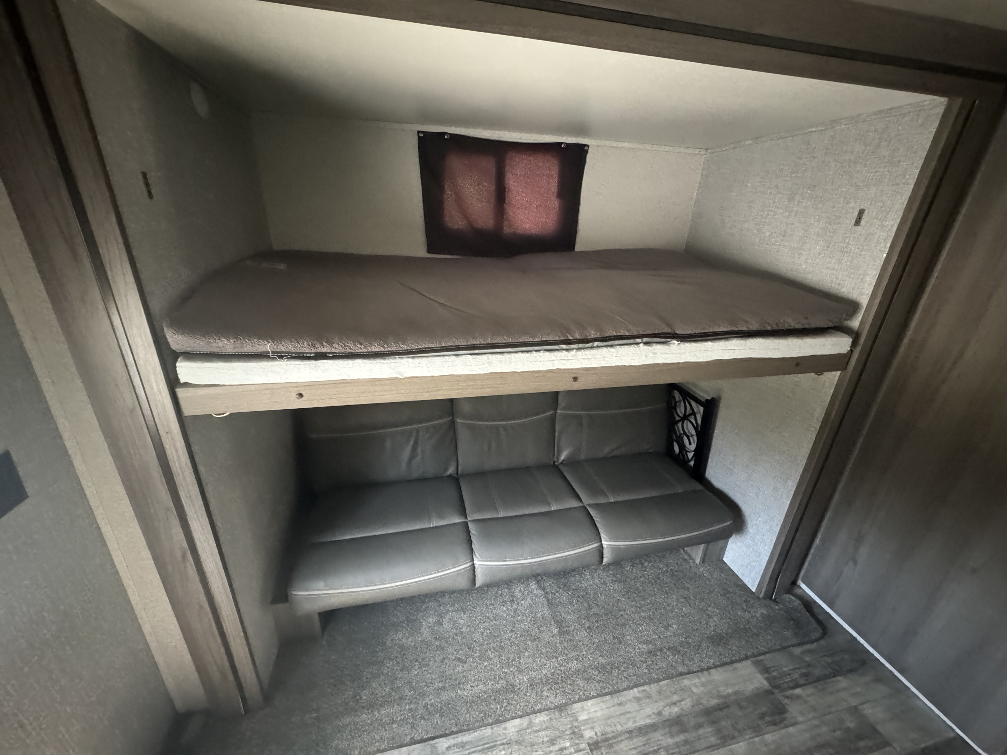 RV rental interior: cozy bunk beds with an upper sleeping area and a gray leather-look convertible sofa below.. Crossroads Volante 2021