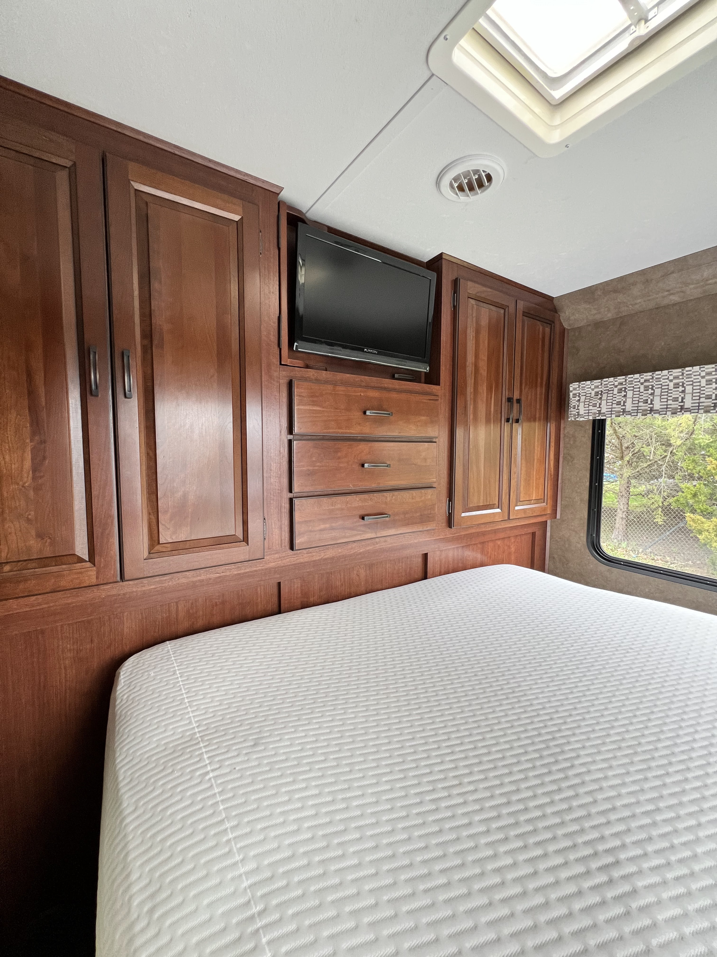 The master bedroom bed is in a pop-out, so there is about 12 inches of walkway at the foot of the bed, when popped. This shot shows the ample storage and TV (And there is storage behind the TV).
This master has a curtain for privacy, but as mentioned, the bathroom door can be opened and locks into place via a magnet to create privacy between the master and main cabin. It's super clever. Have we mentioned it is super clever?. Forest River Sunseeker 2016