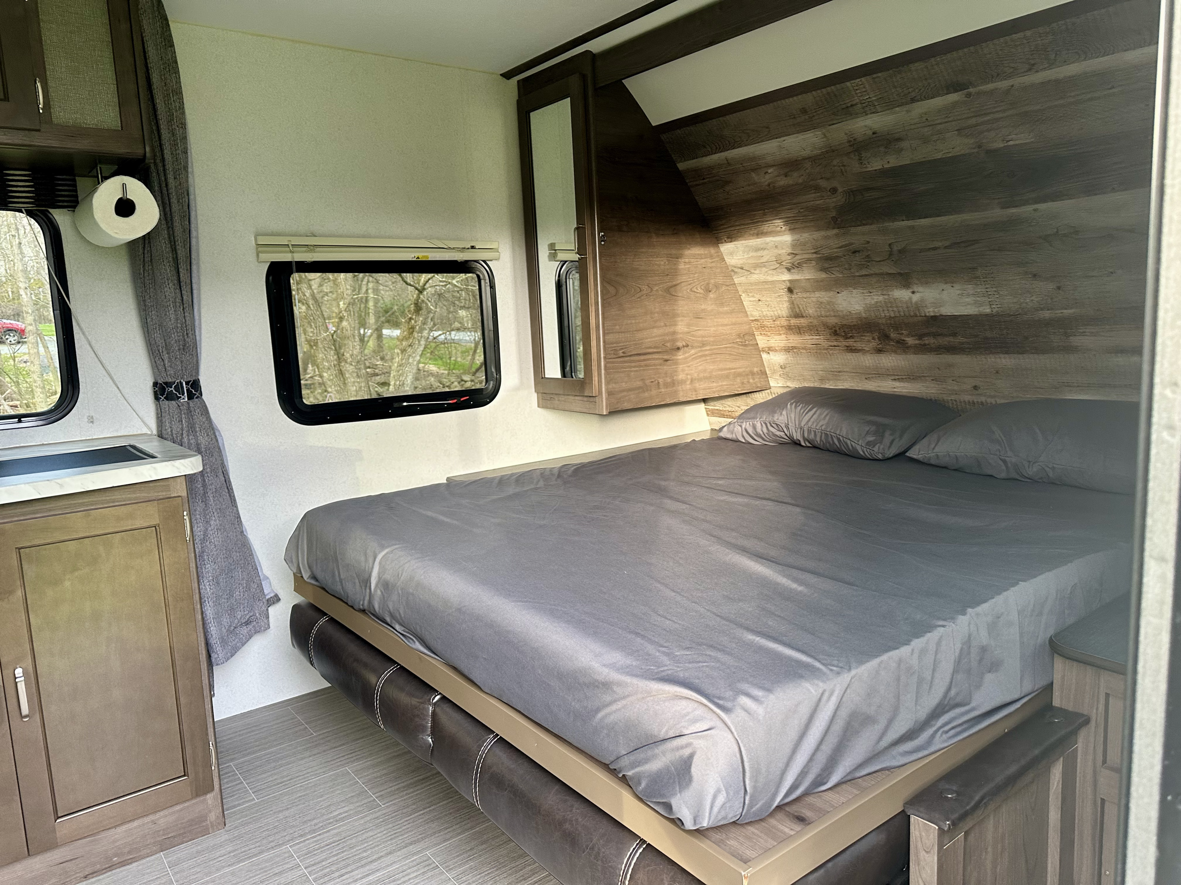 Experience a comfortable RV rental interior featuring a spacious bed, compact kitchen area with sink, and scenic windows.. Keystone RV Passport Express 2019