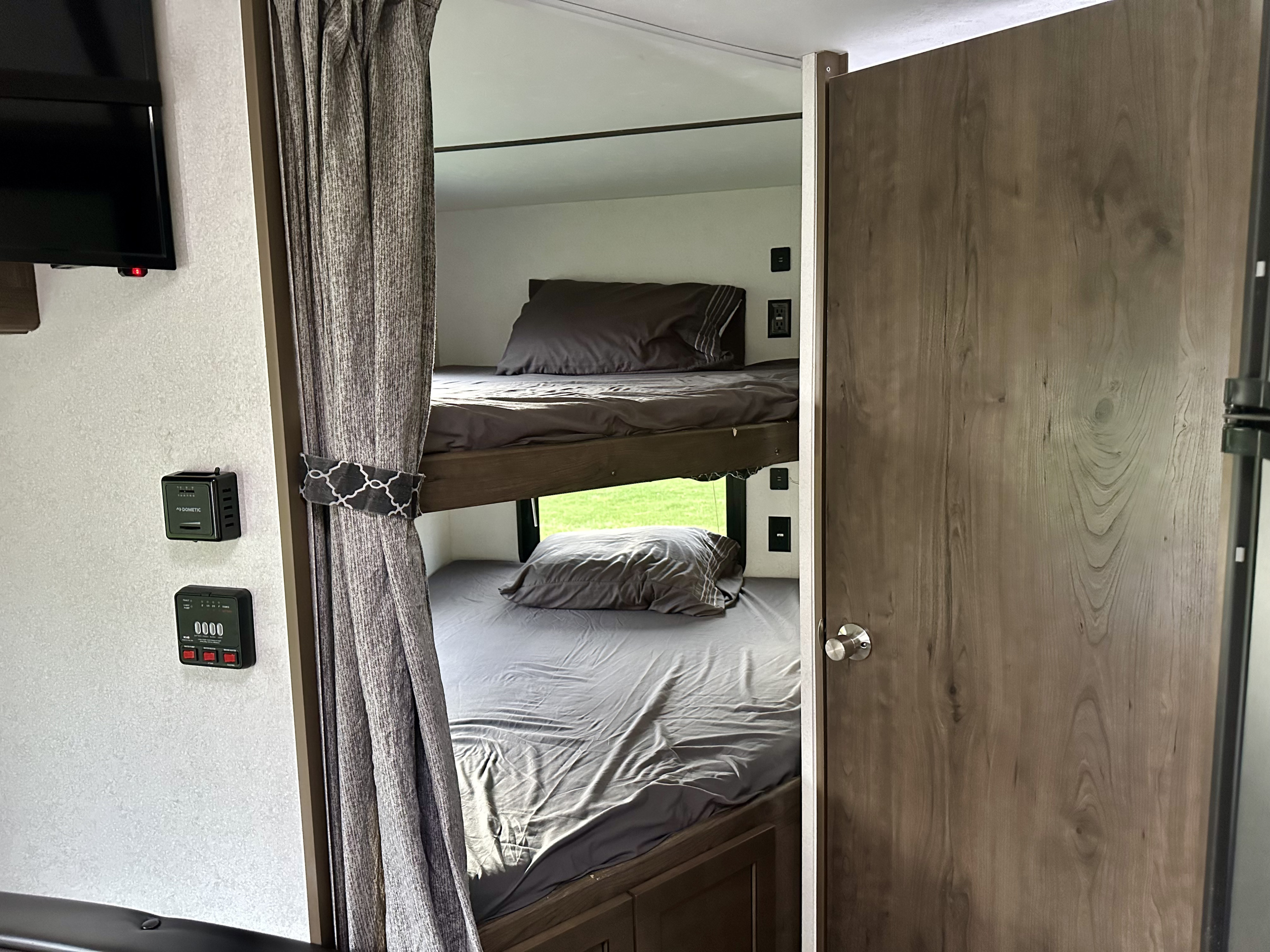Interior view of an **RV rental** showing modern bunk beds with grey bedding, a privacy curtain, and control panels.. Keystone RV Passport Express 2019