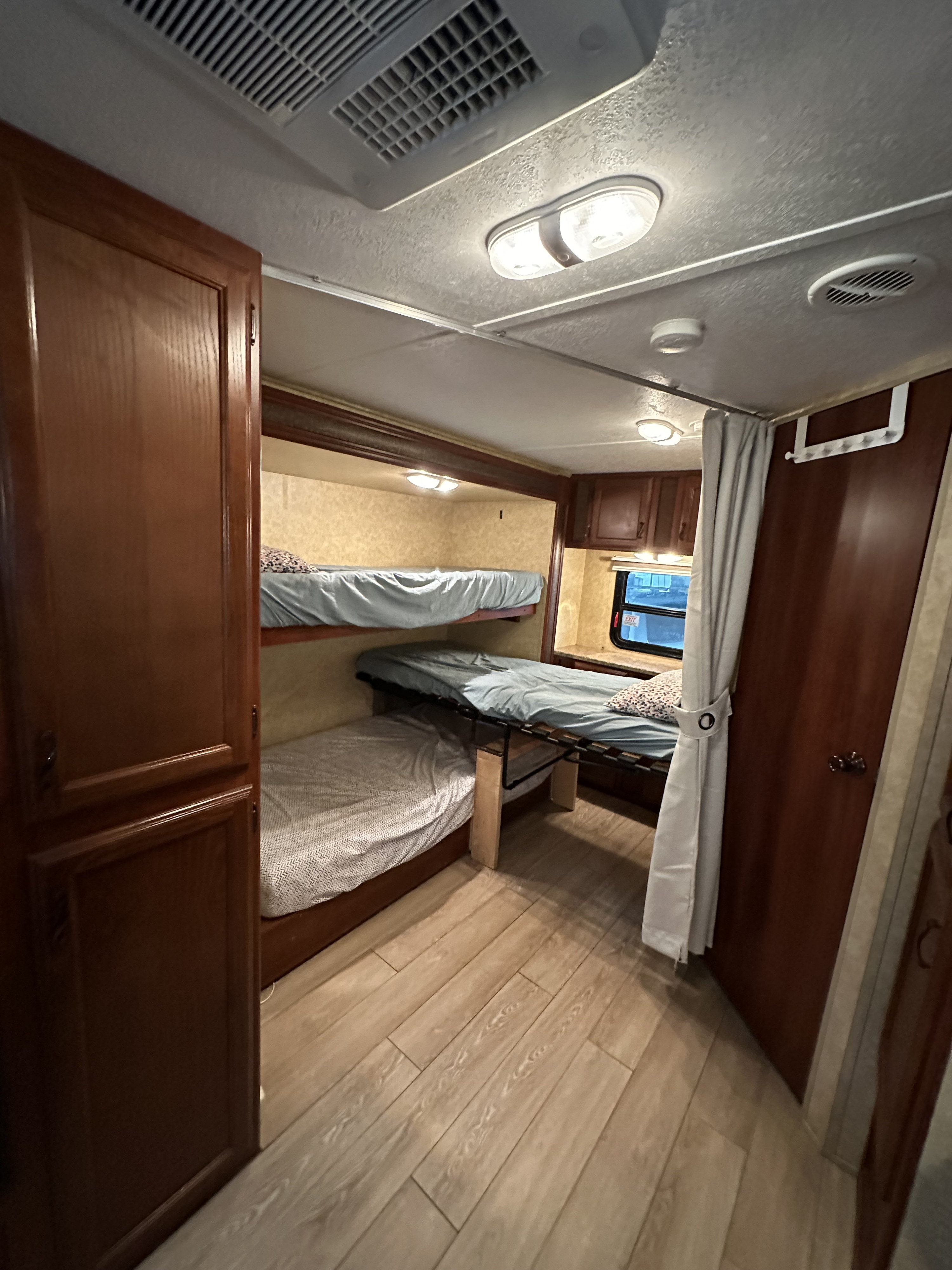 RV rental interior featuring comfortable bunk beds, light wood flooring, and overhead lighting. Ideal for family travel accommodations.. Forest River Tracer Executive 2010
