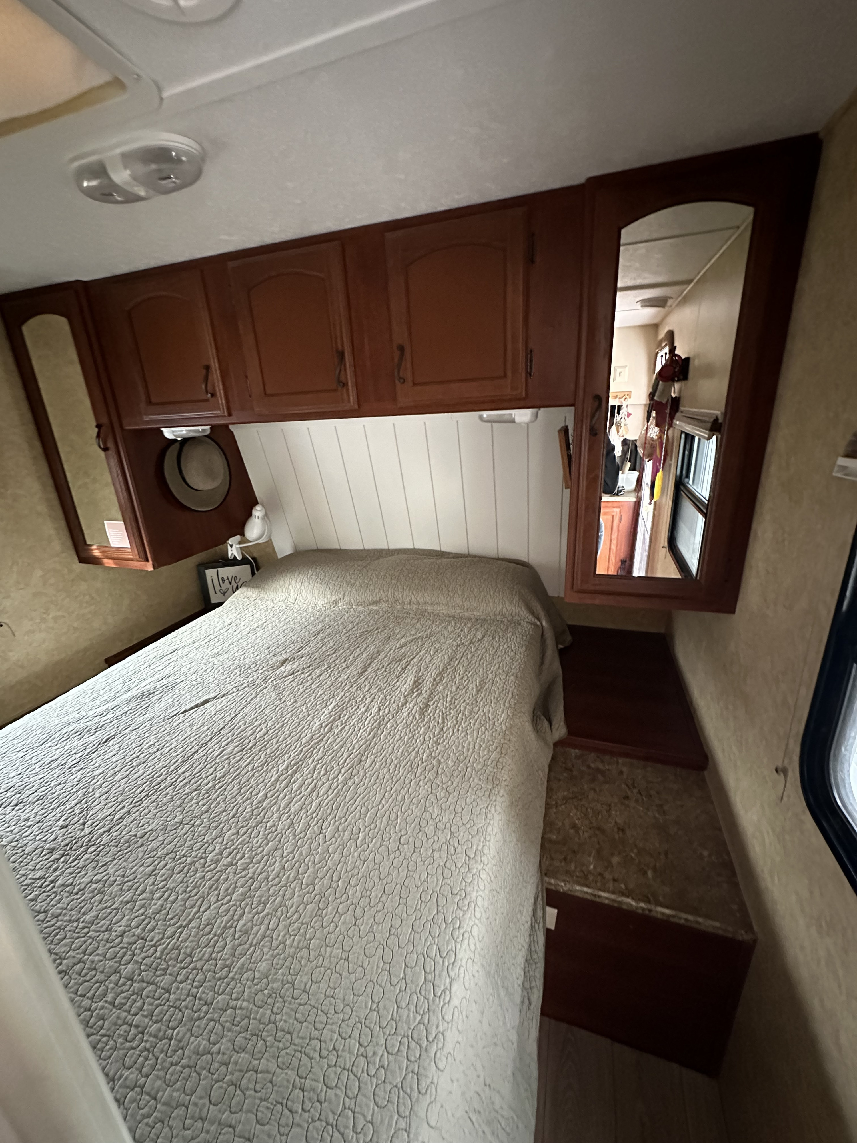 Compact RV rental bedroom with a quilted bed, wooden overhead cabinets, and built-in mirrors. Cozy travel space.. Forest River Tracer Executive 2010