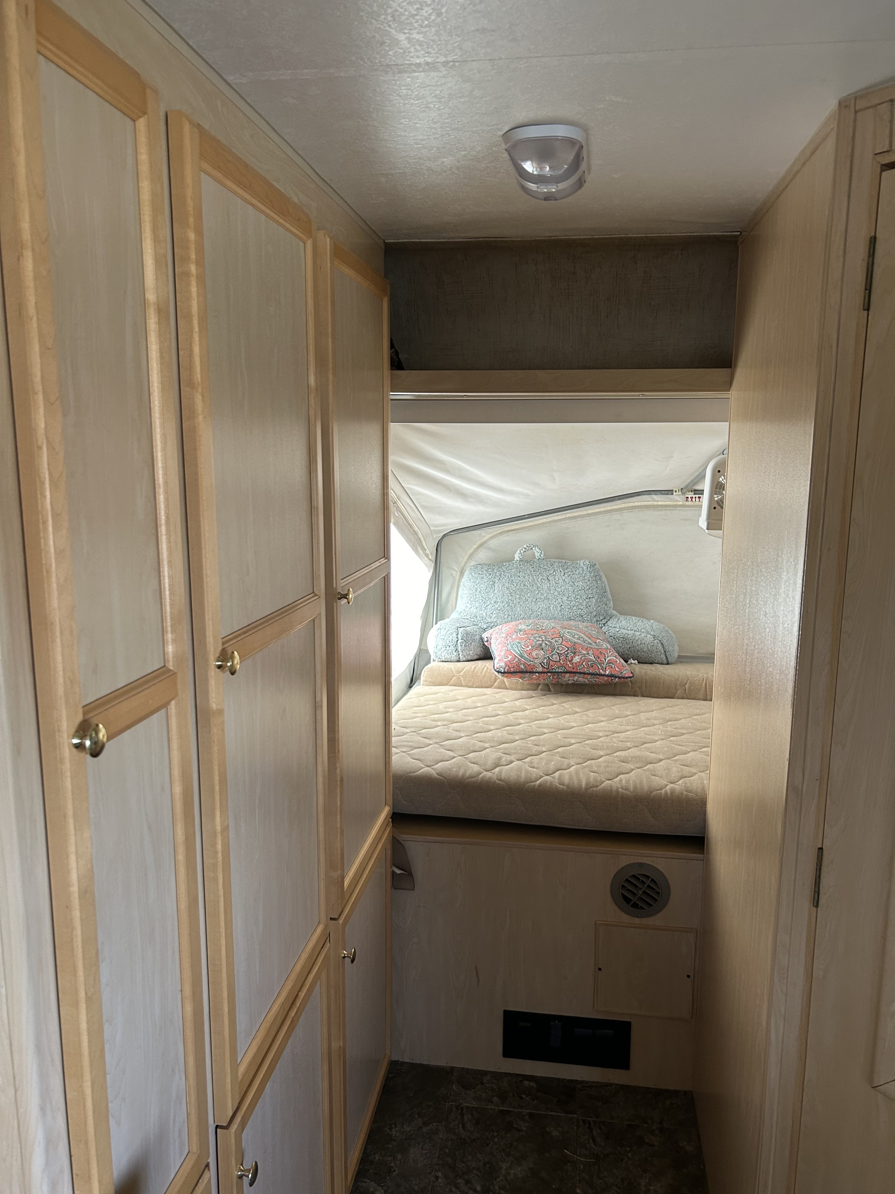 Inside an RV rental: a hallway with light wood cabinets on the left, leading to a bed with pillows under a pop-up tent section.. Jayco Jay Feather EXP 2004
