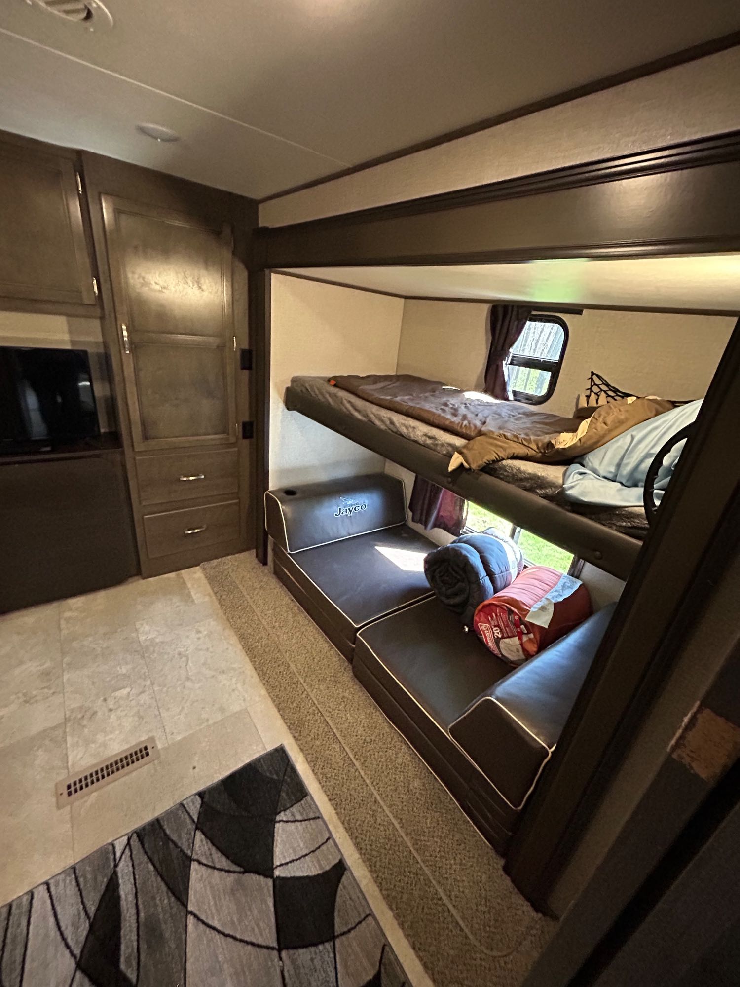 View inside an RV rental, featuring bunk beds, a lower sofa/bed, and cabinet storage. A practical camper interior for travel.. Jayco Jay Flight 2020