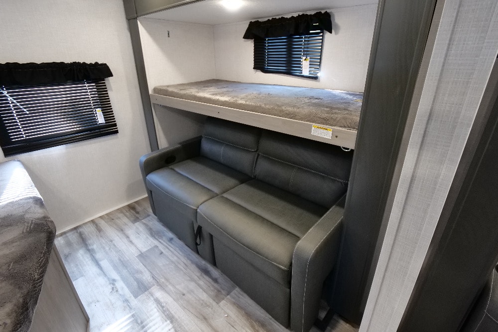 RV rental interior: bunk bed over a sofa sleeper, with windows, blinds, and light wood-look flooring.. Dutchmen Coleman Light 2022