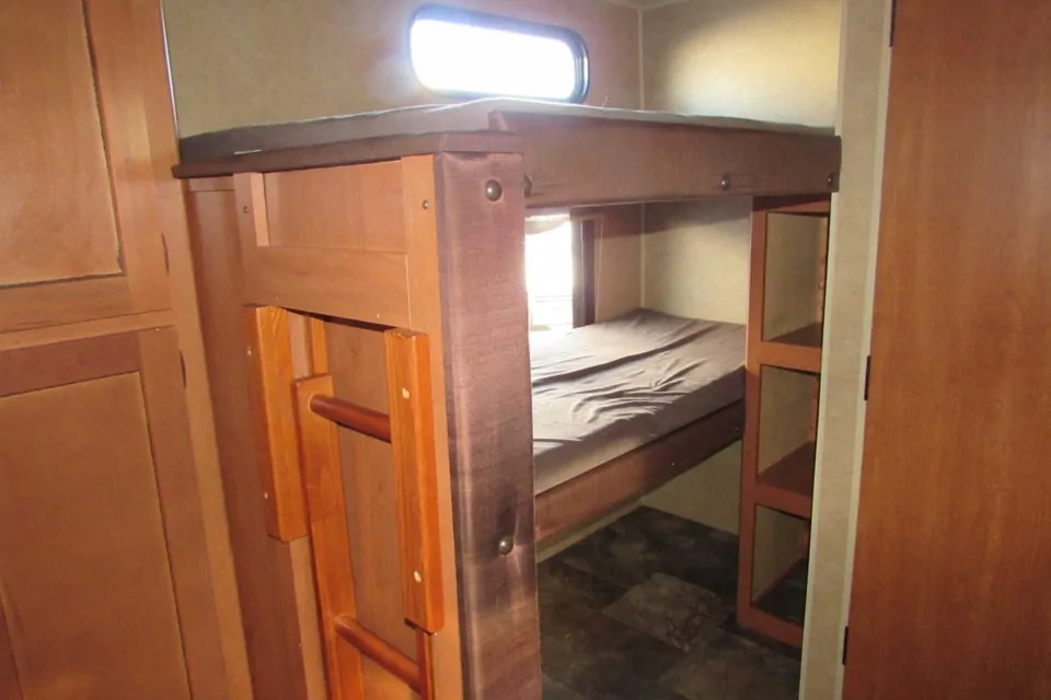 RV rental bunk beds: A cozy sleeping area with a ladder, window, and built-in storage shelves.. Forest River Cherokee Grey Wolf 2014