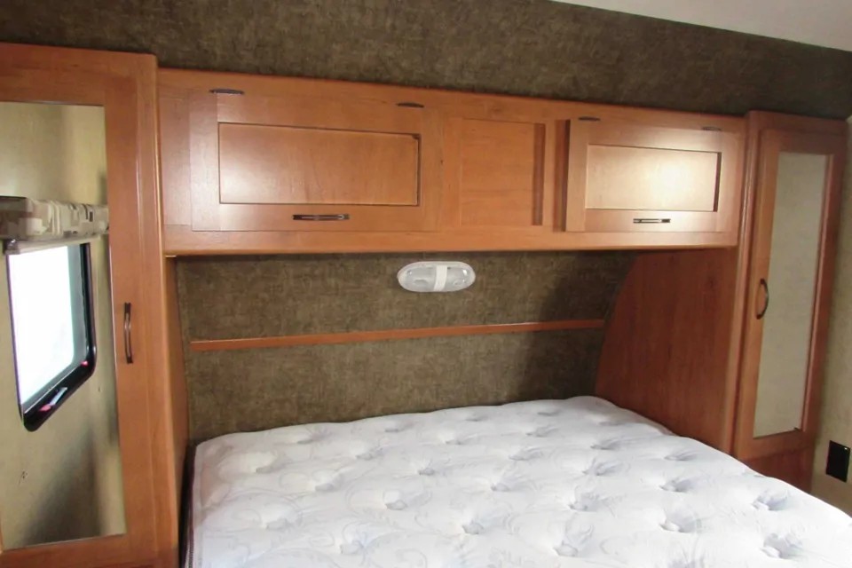 Cozy RV rental bedroom showing a white mattress, overhead cabinets, and a window.. Forest River Cherokee Grey Wolf 2014