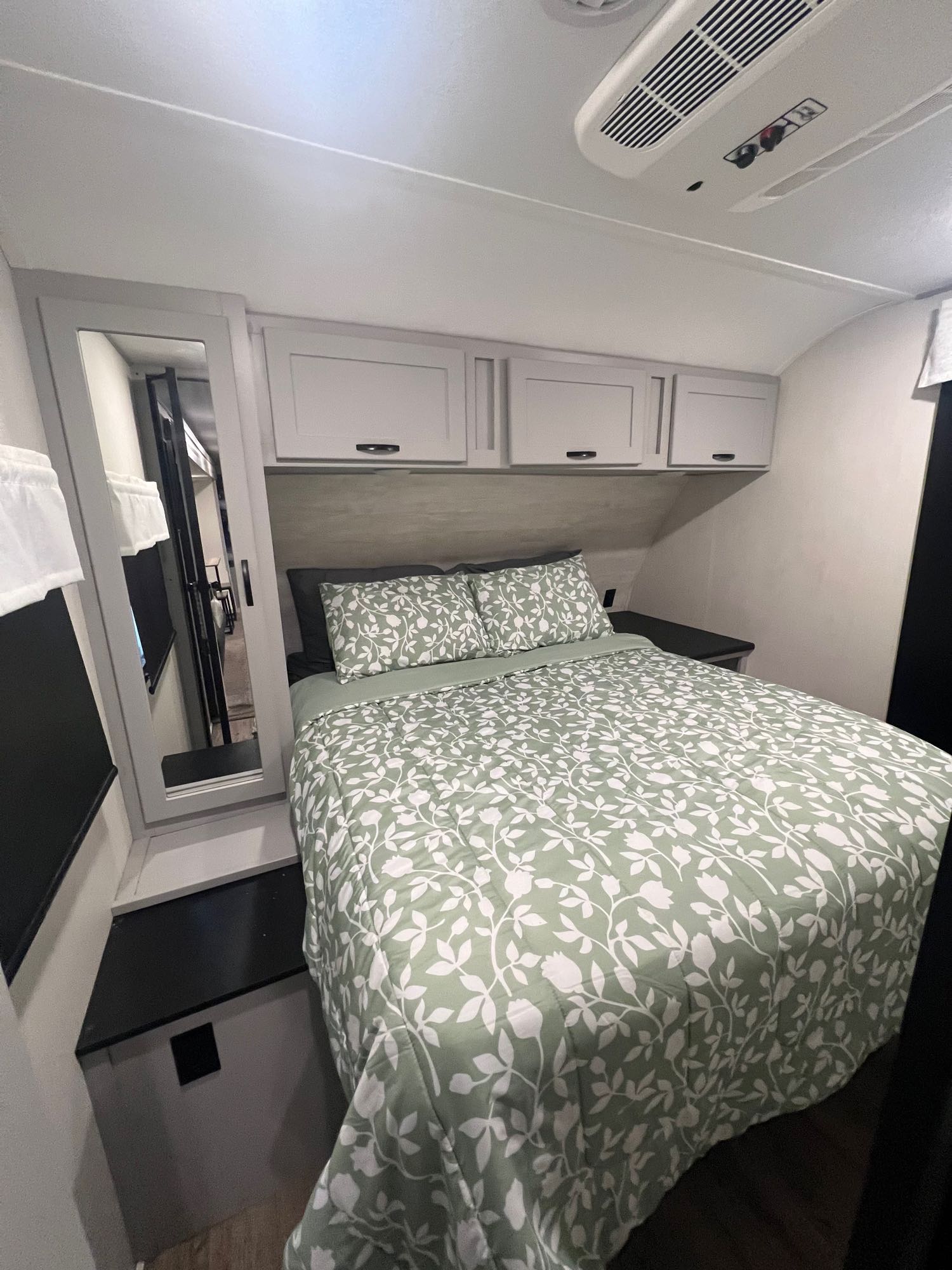 Cozy RV rental bedroom with floral bedding, overhead cabinets, and AC. Perfect for compact travel comfort.. Forest River Vibe 2021
