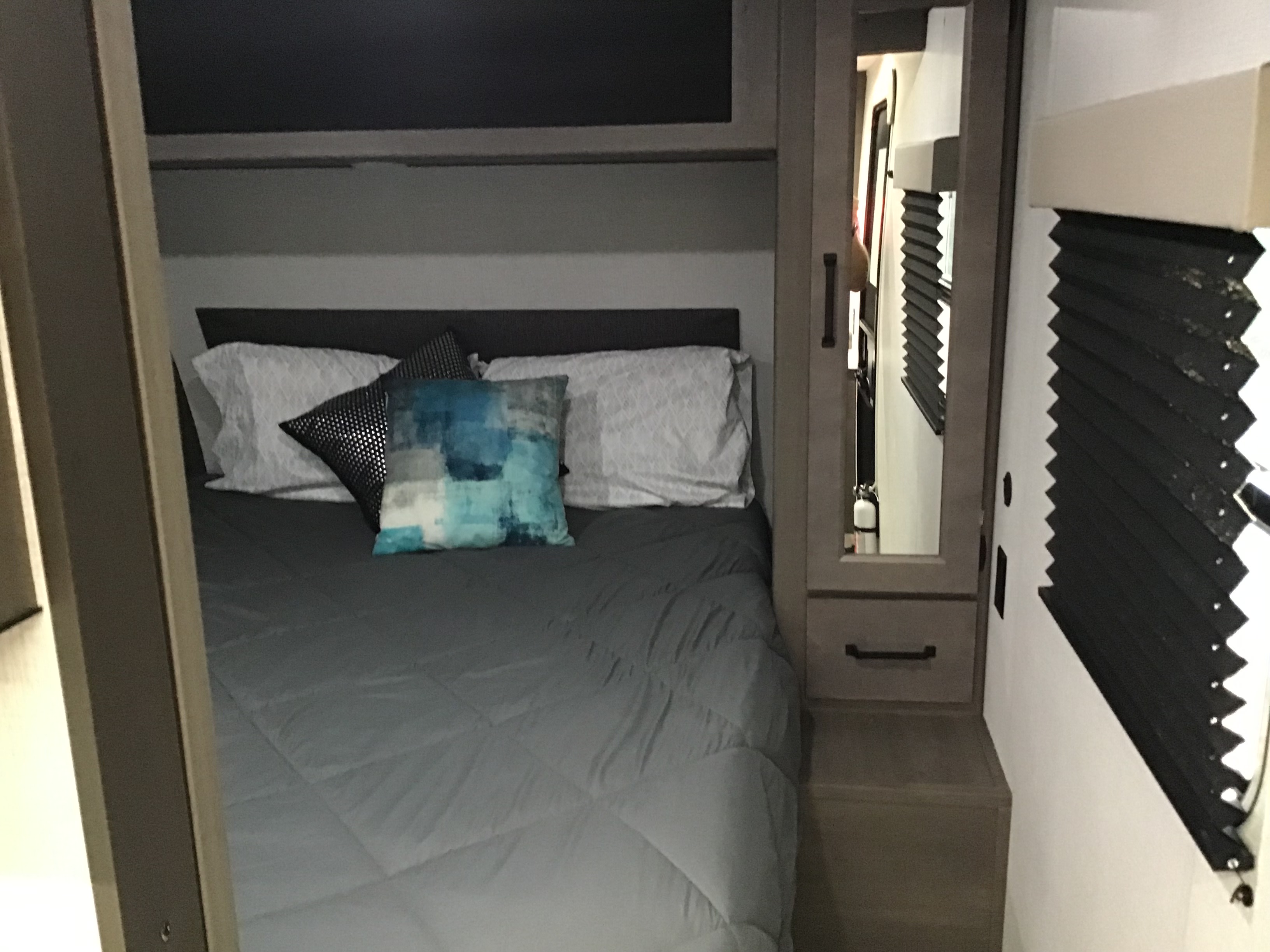 Cozy RV rental bedroom features a comfy bed, accent pillows, mirrored closet, and pleated window blinds.. Grand Design Transcend Xplor 2024