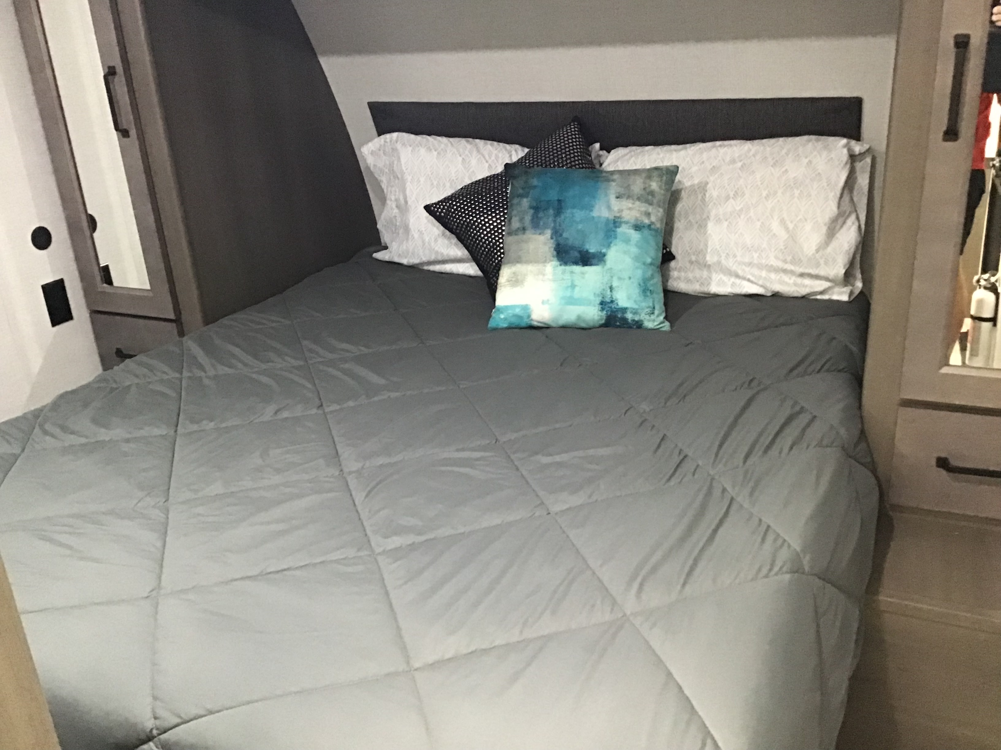 RV rental bedroom: A comfortable bed with a grey comforter, white pillows, and blue accent pillow in a cozy interior space.. Grand Design Transcend Xplor 2024
