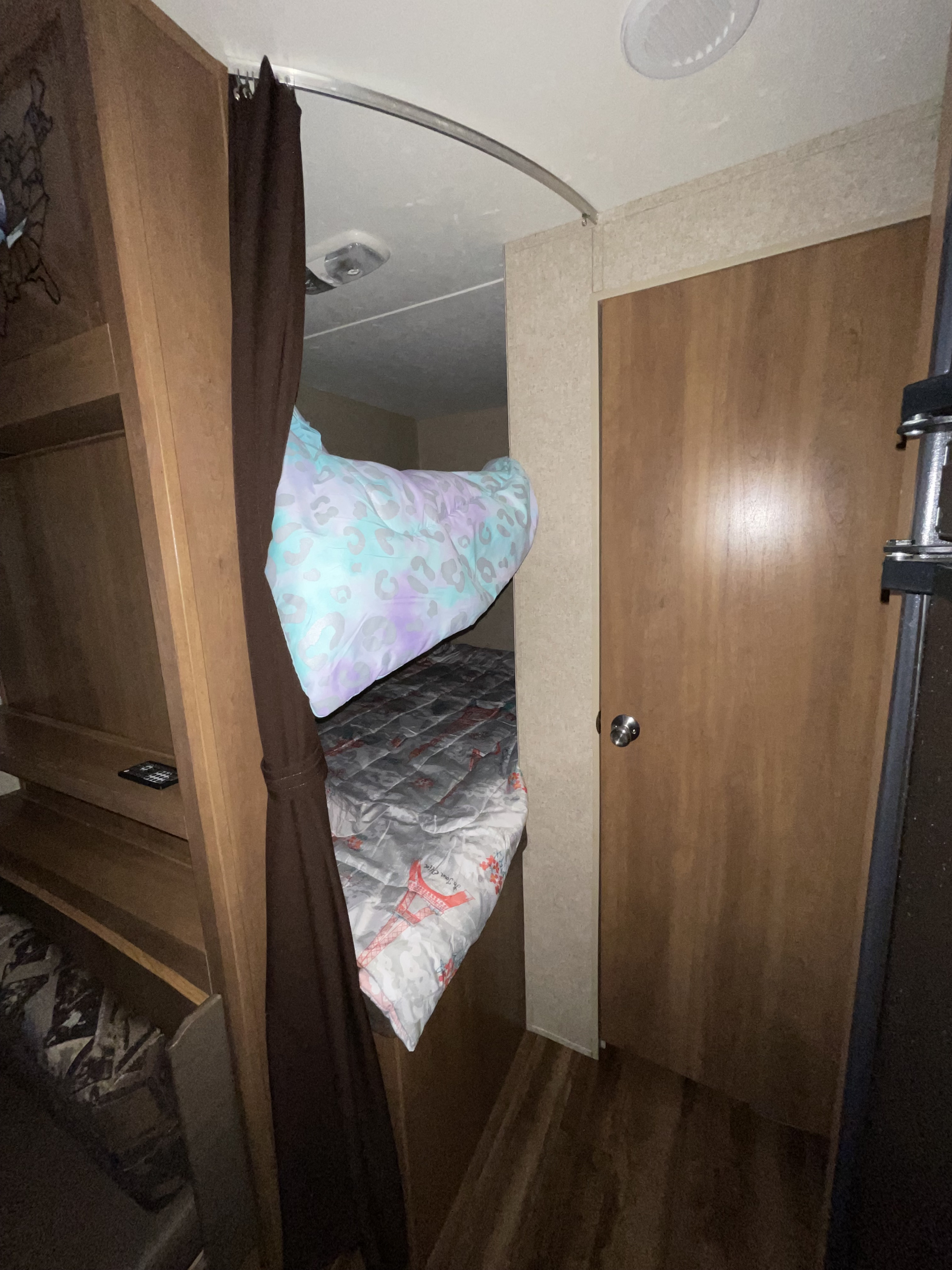 An RV rental features bunk beds with a patterned blue top comforter, gray lower one, and privacy curtain.. Coachmen 273bh 2017