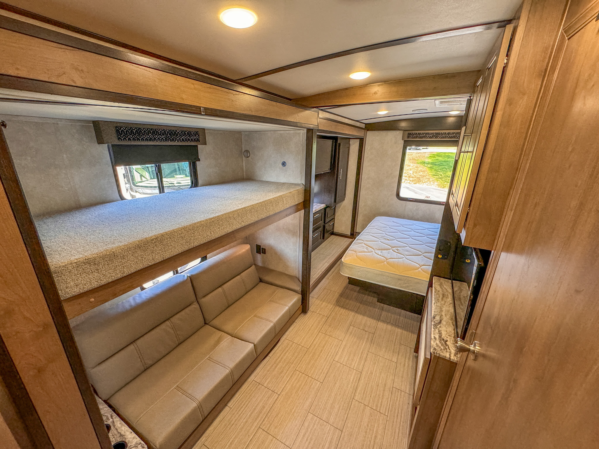 RV rental interior: a bedroom with bunk beds, a sofa below, and a queen bed. Features wood cabinetry and tiled floor.. Forest River Fr3 2021