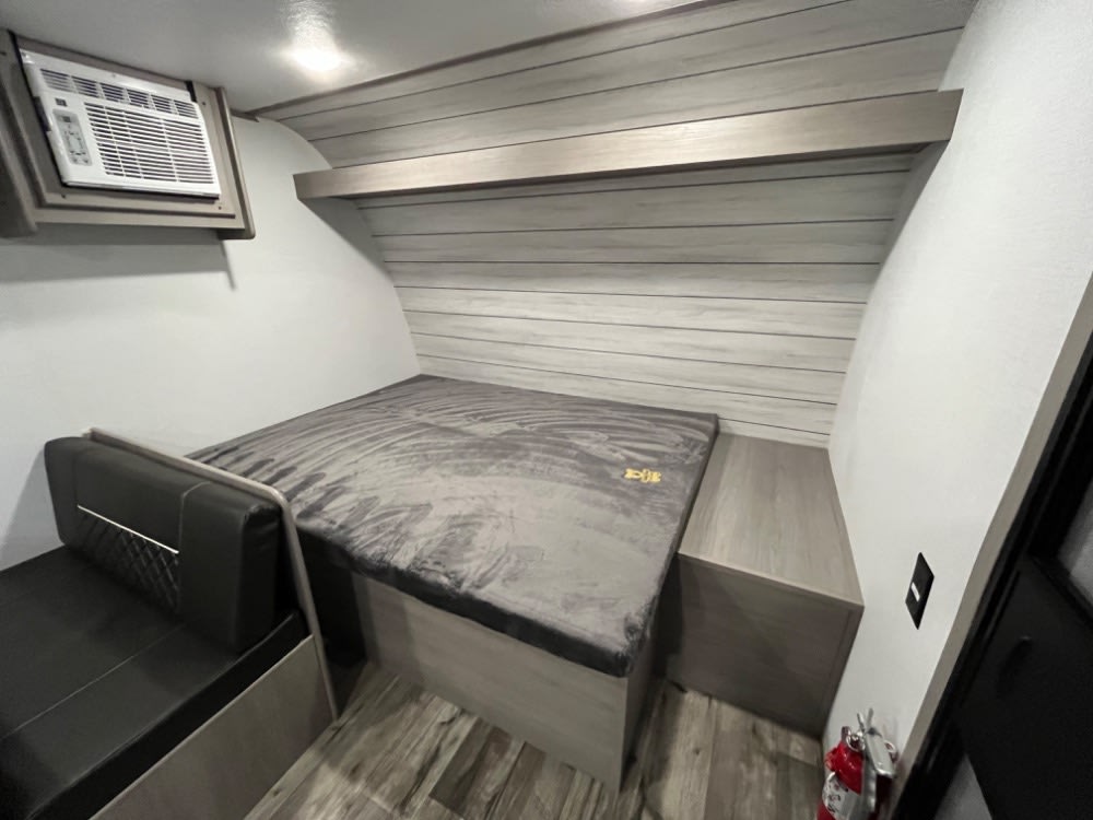 This RV rental interior shows a cozy bed, AC, black bench, and wood-paneled walls, ready for camping.. Coleman Lantern LT 17 B 2024