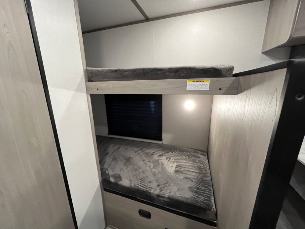 This RV rental interior features two comfortable bunk beds with mattresses and a window, ideal for family travel.. Coleman Lantern LT 17 B 2024
