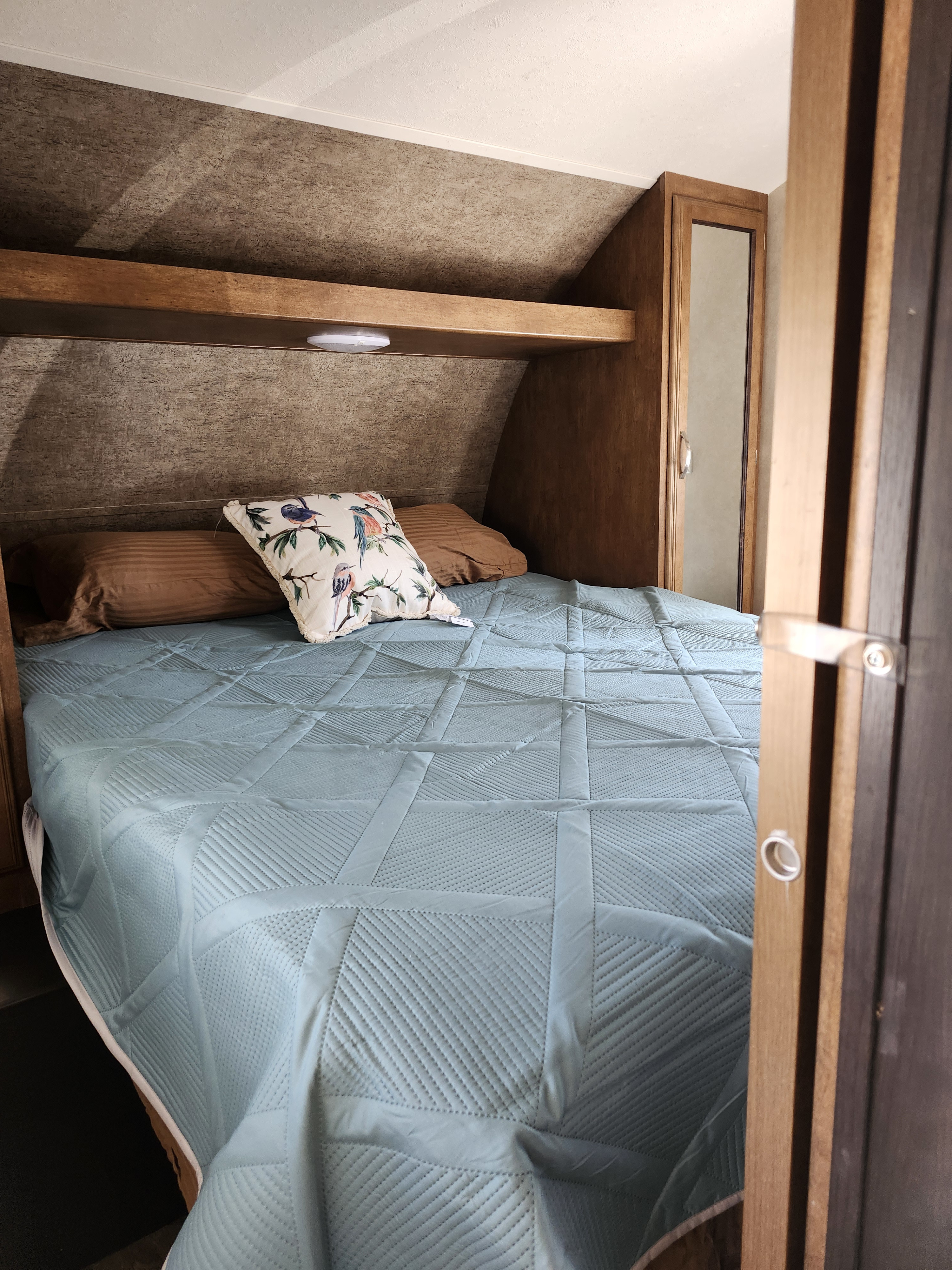 Inside an RV rental: a cozy bedroom with a light blue quilted bedspread, brown pillows, and built-in storage.. Forest River Salem Cruise Lite 2017