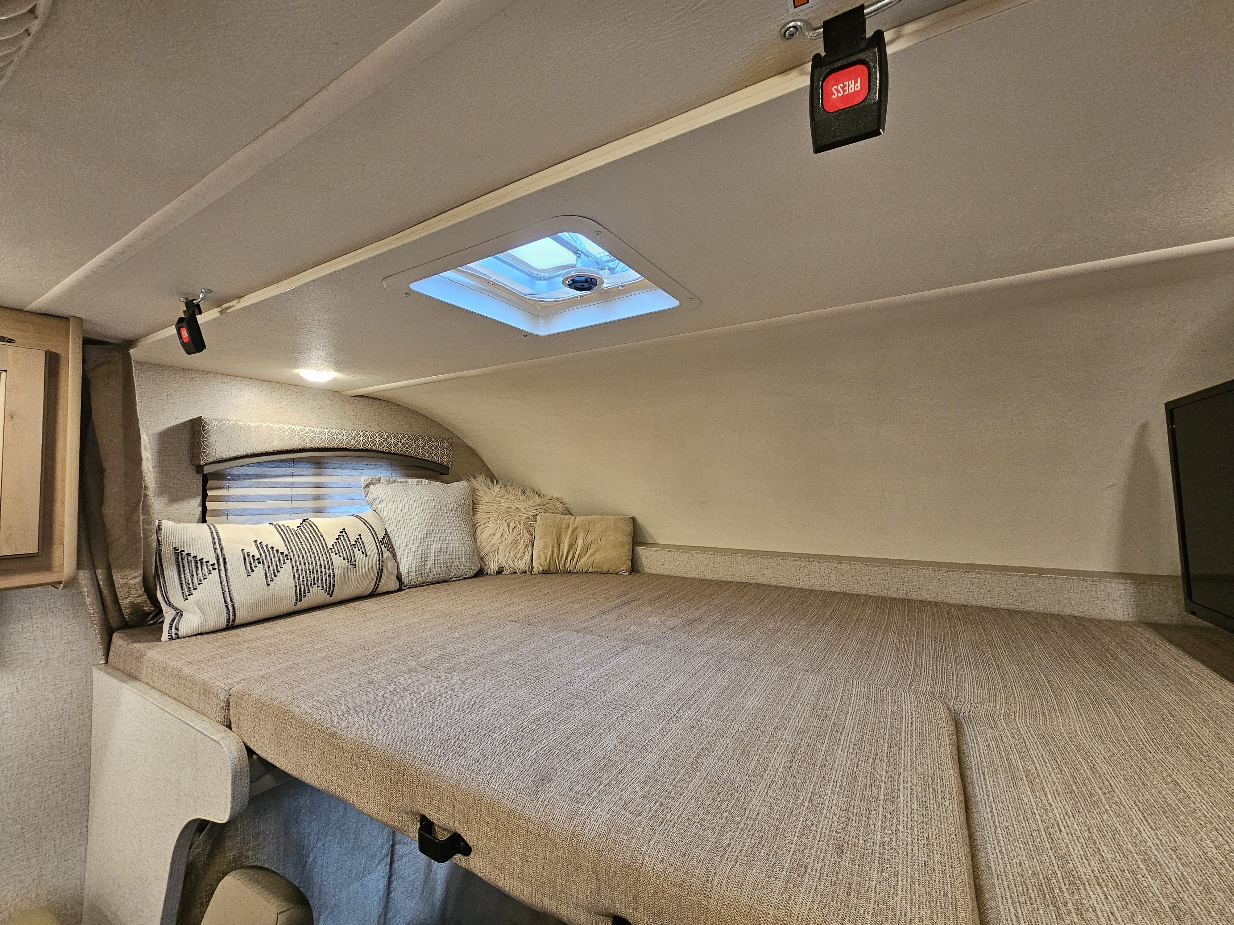 Inside an RV rental: a spacious cab-over bed with comfy pillows, a skylight, & safety clip.. Thor Motor Coach Four Winds 2021