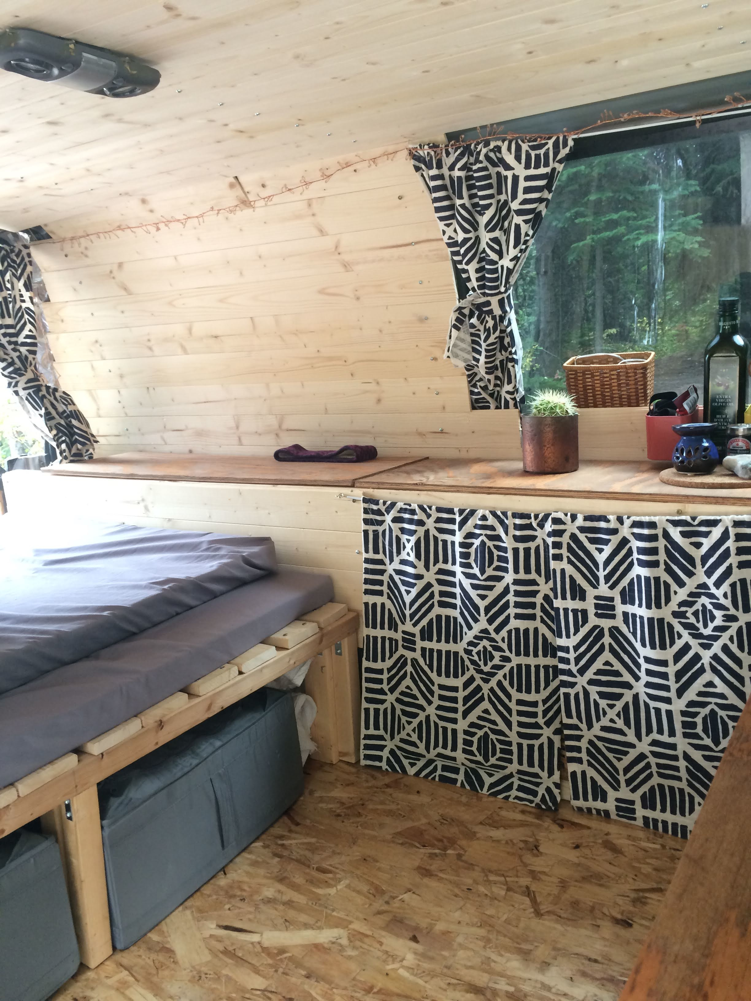 Cozy rv rental interior featuring a bed, wooden paneling, and a window overlooking trees. Includes practical storage and small counter space.. GMC Safari 2002