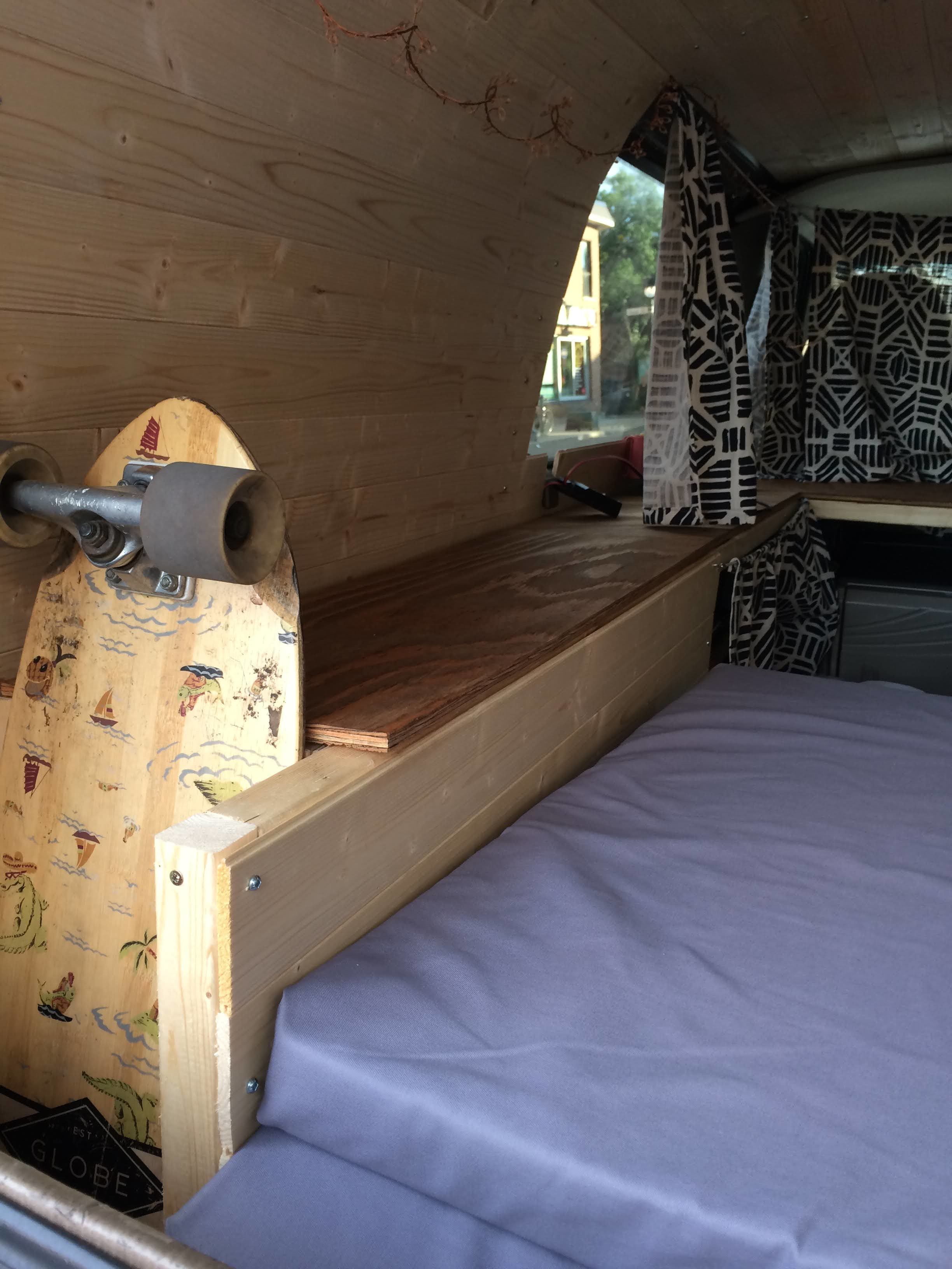 Cozy RV rental interior with wood paneling, a comfy bed, and a longboard, perfect for travel.. GMC Safari 2002