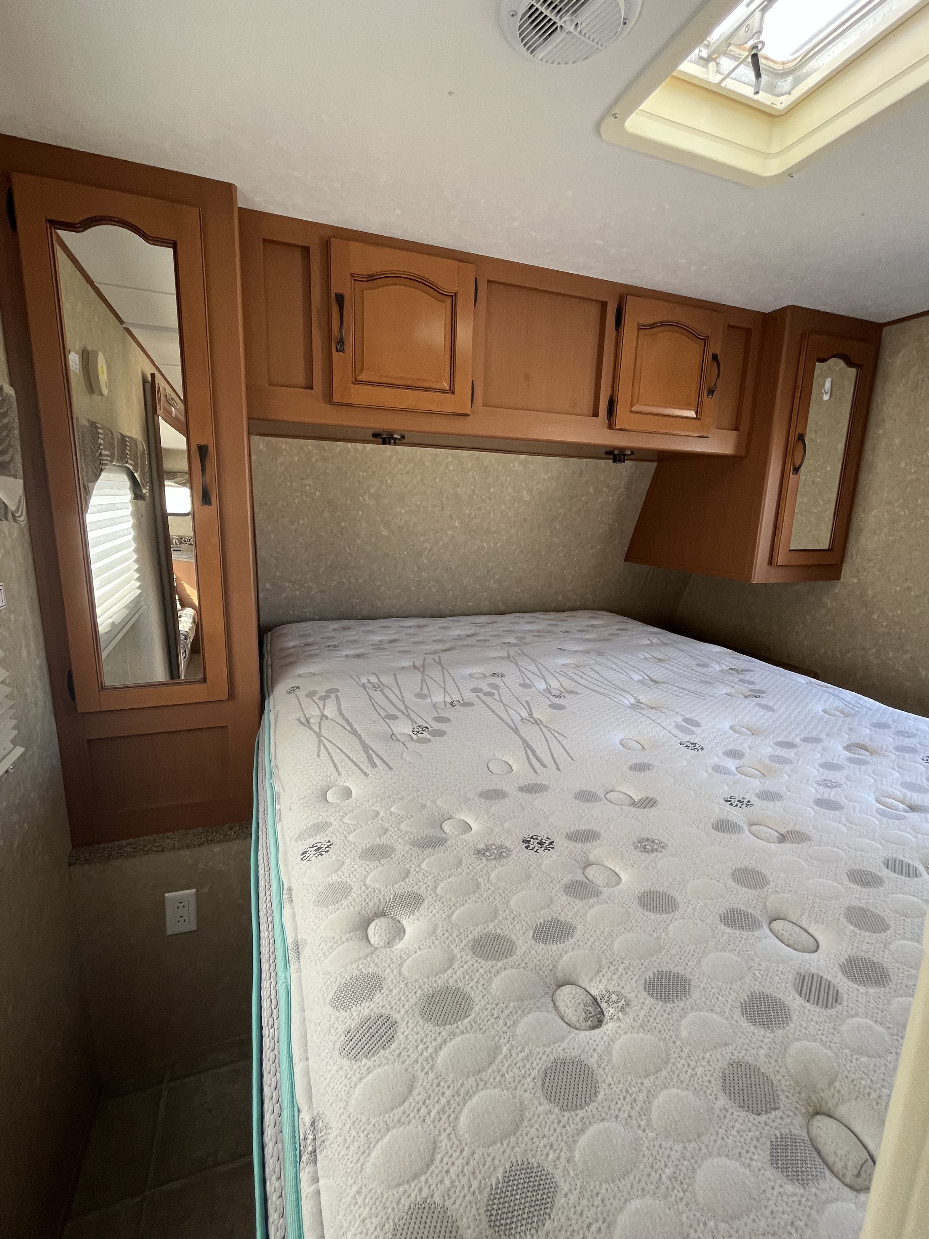 Inside this RV rental, a comfy bedroom awaits with a patterned mattress, wooden overhead cabinets, and a ceiling skylight.. Gulf Stream Emerald Bay 2009