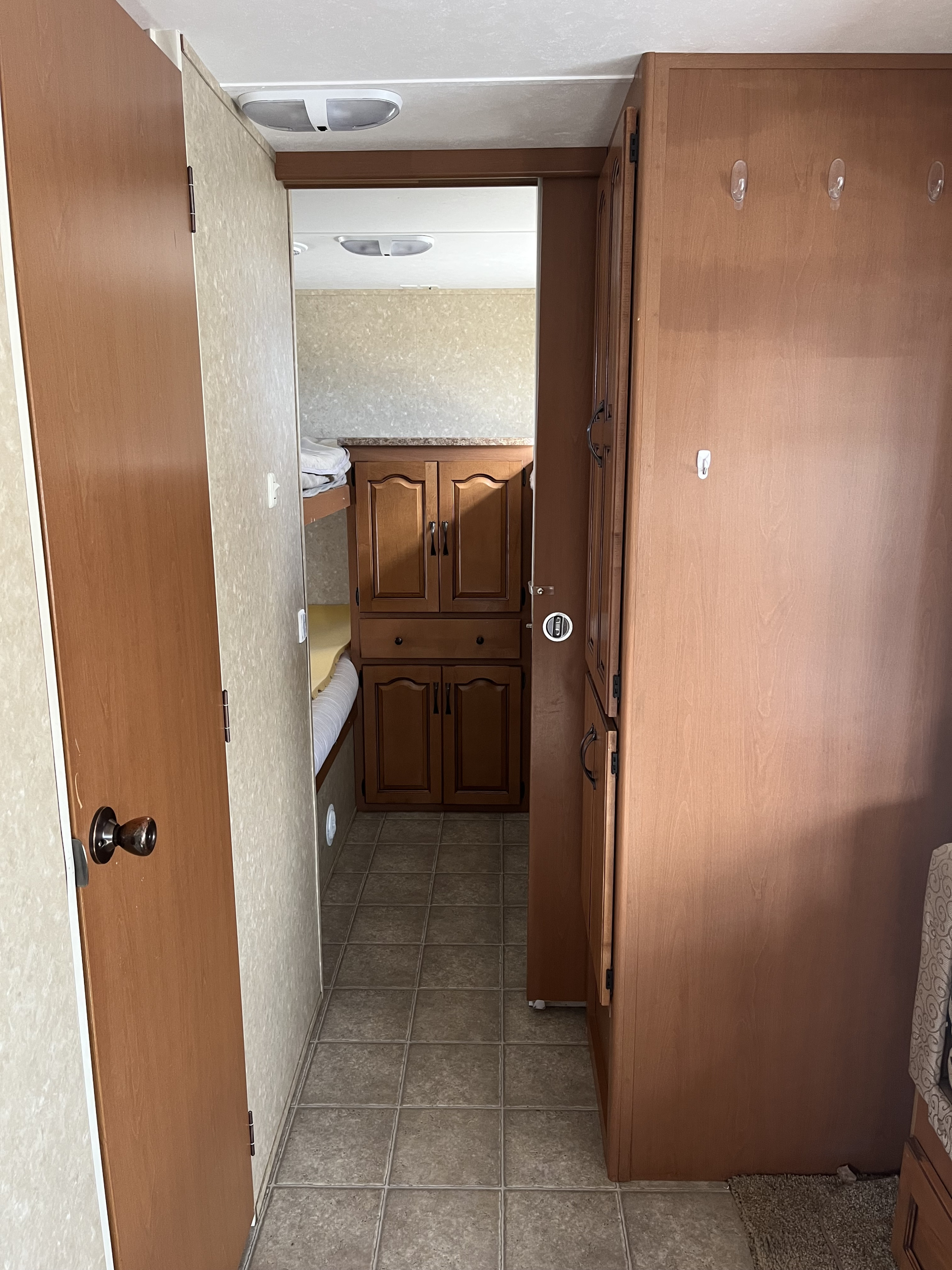 RV rental compact interior hallway with wood storage cabinets, a door, and a glimpse of the bunk area, featuring light-toned walls.. Gulf Stream Emerald Bay 2009