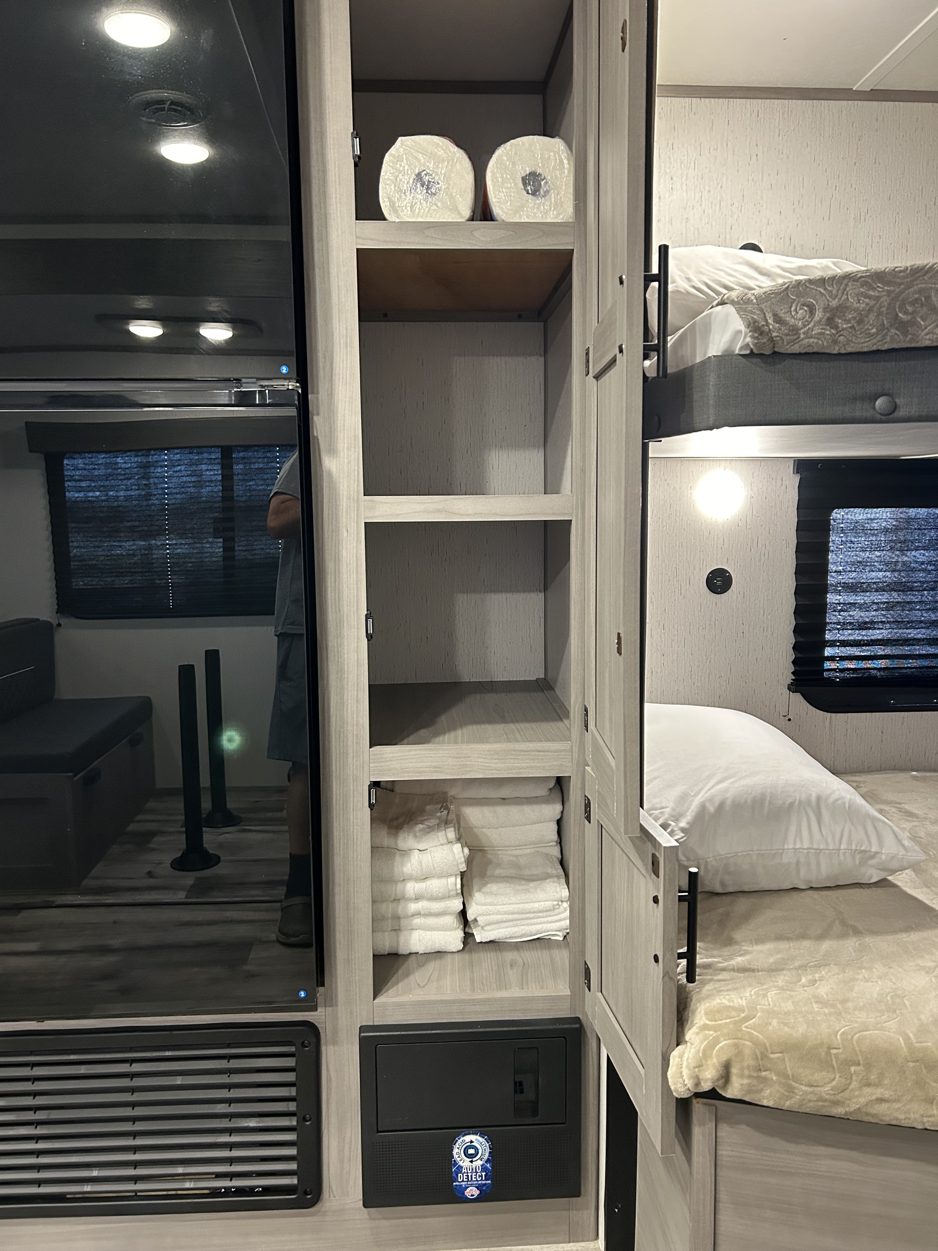 An RV rental's cozy bunk area with beds and a cabinet stocked with towels & paper towels. A power panel is visible below.. Dutchmen Coleman Lantern LT 2023