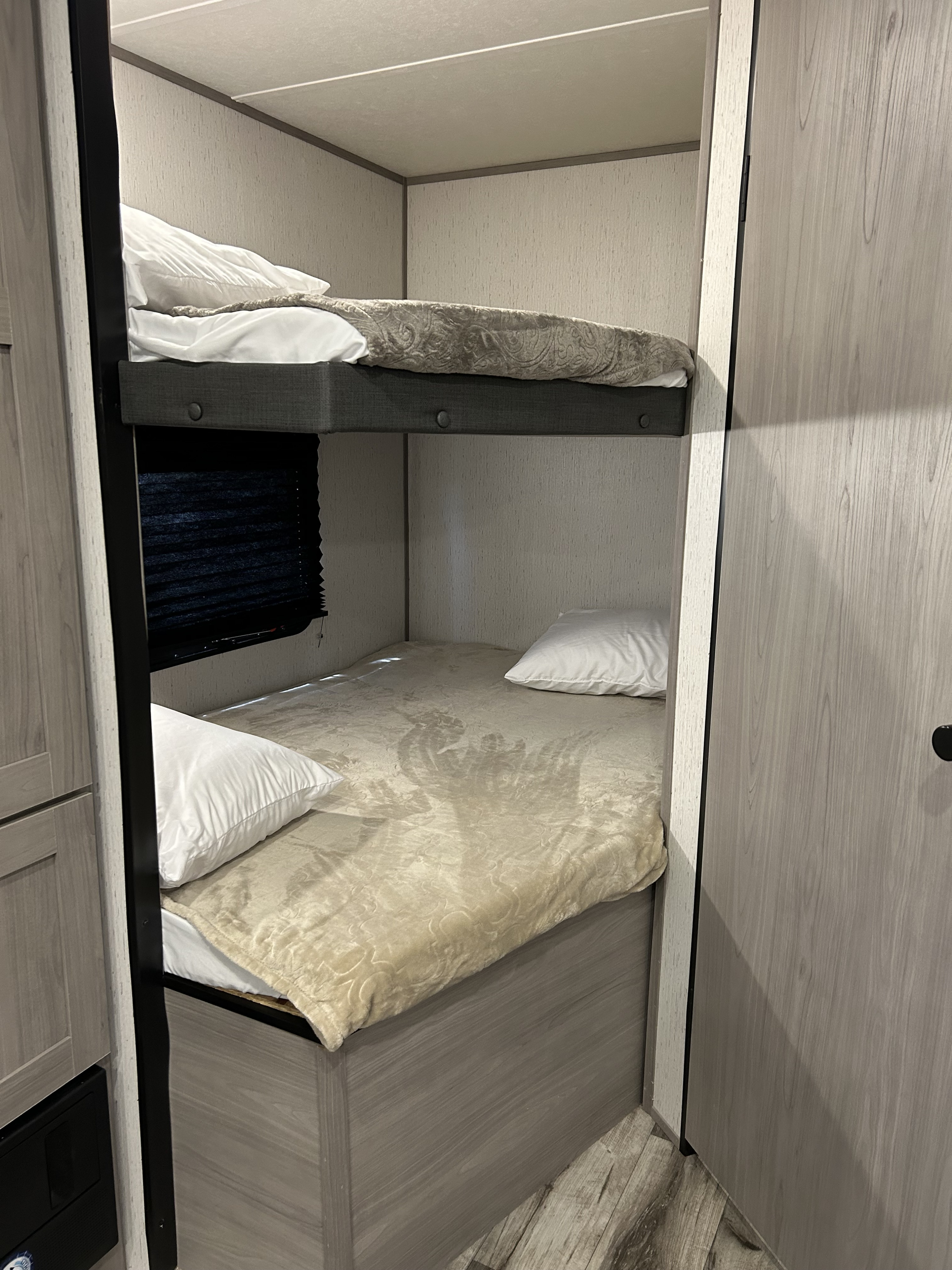 Upper and lower bunk beds in a cozy RV rental, made with white linens and patterned blankets.. Dutchmen Coleman Lantern LT 2023