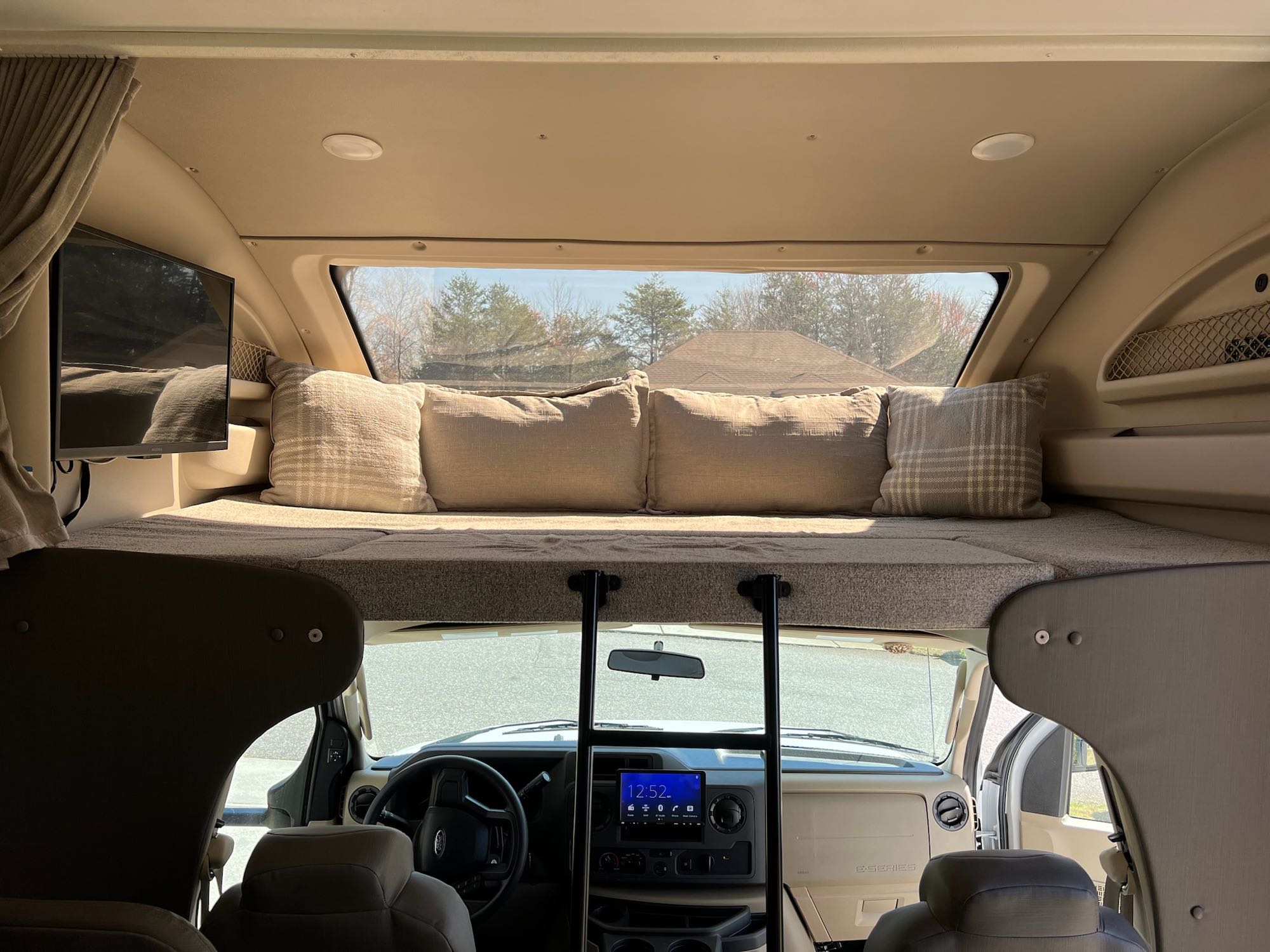 RV rental interior, showing comfy over-cab bunk, TV, and driver's dashboard with a clear front view.. Entegra Coach Odyssey 2021