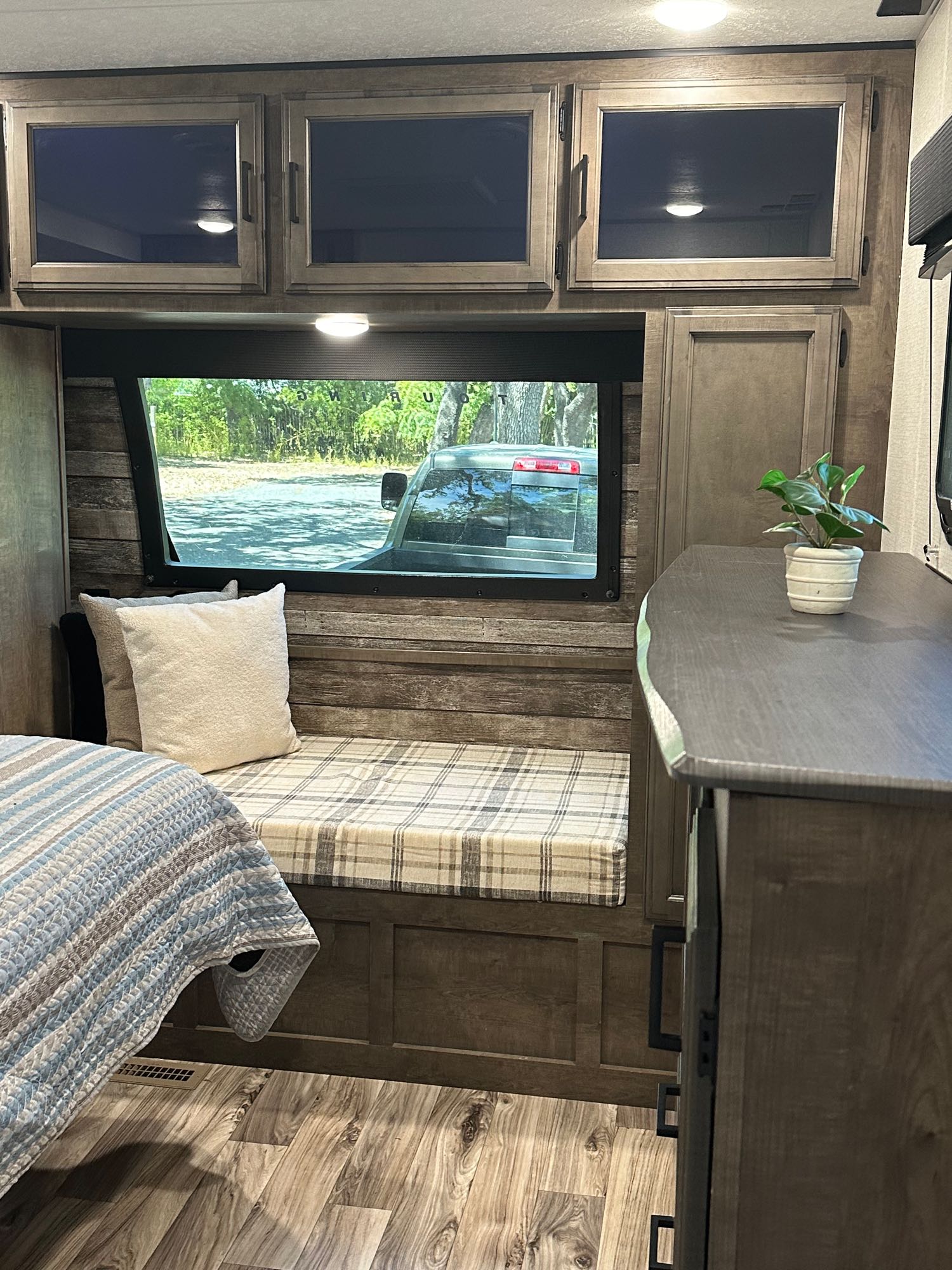 Spacious rv rental interior showing a bed, plaid bench, wood cabinets, and a window view of a truck & trees.. Venture STT343VIB 2022