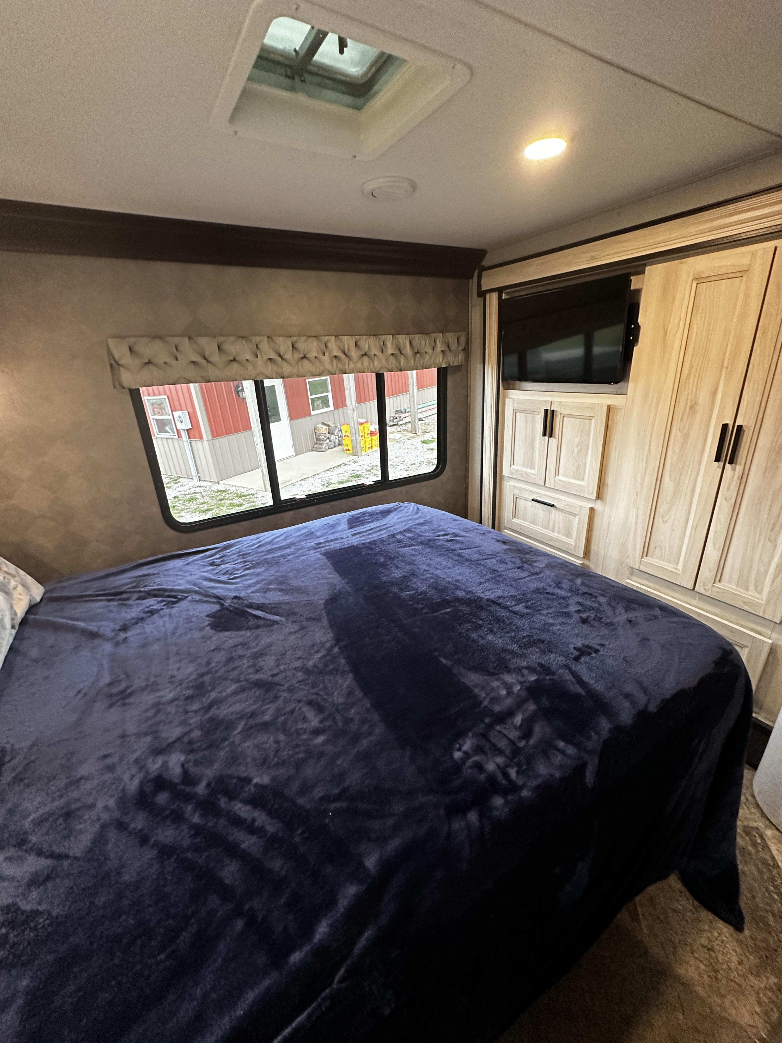 RV rental bedroom interior showing a neatly made bed with dark blue blanket, window, and wood cabinetry with TV.. Forest River Sunseeker 2020