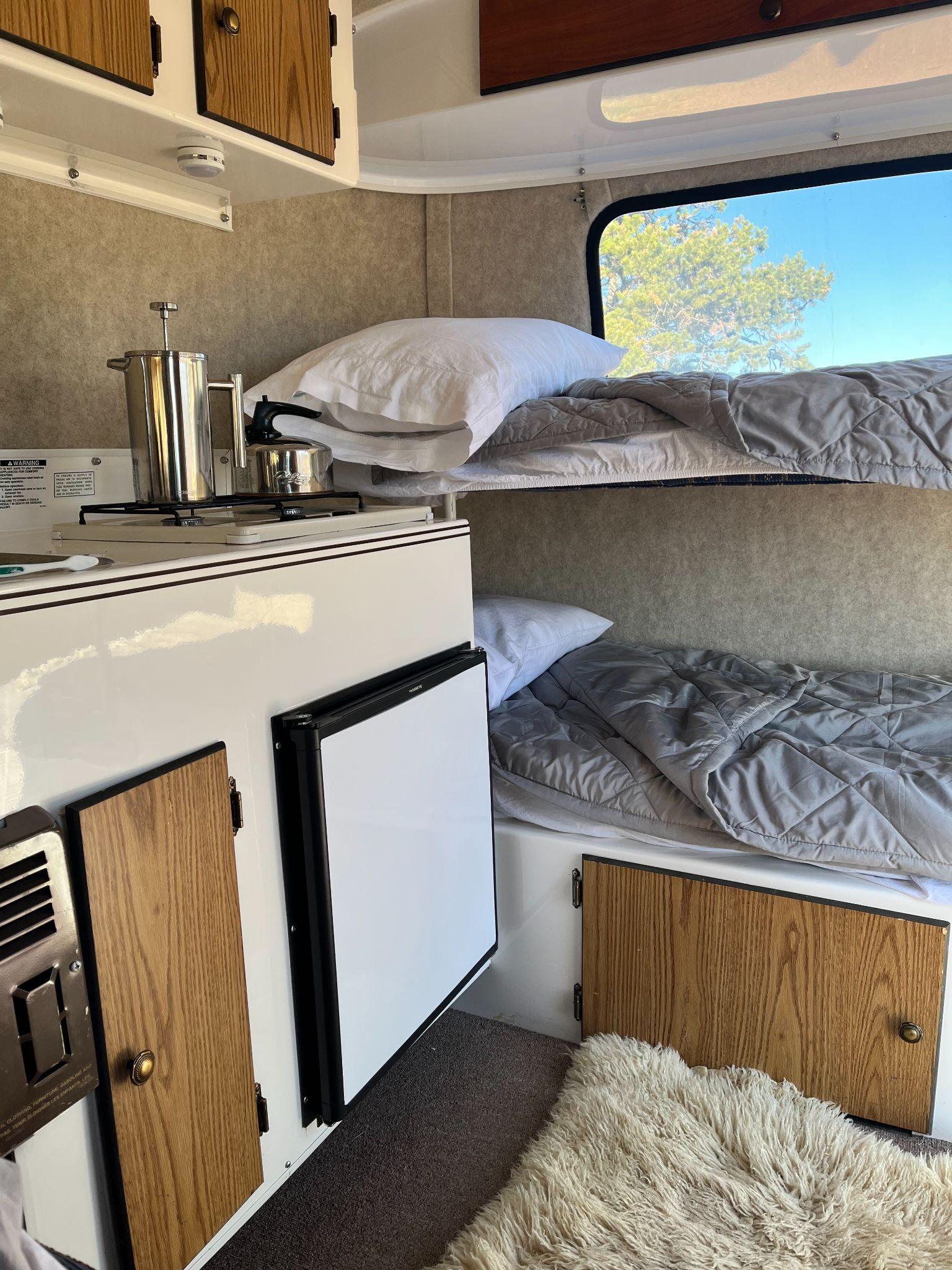 Compact RV rental interior featuring bunk beds, a small kitchen, and fridge for cozy adventures.. Scamp Scamp Trailer 2004