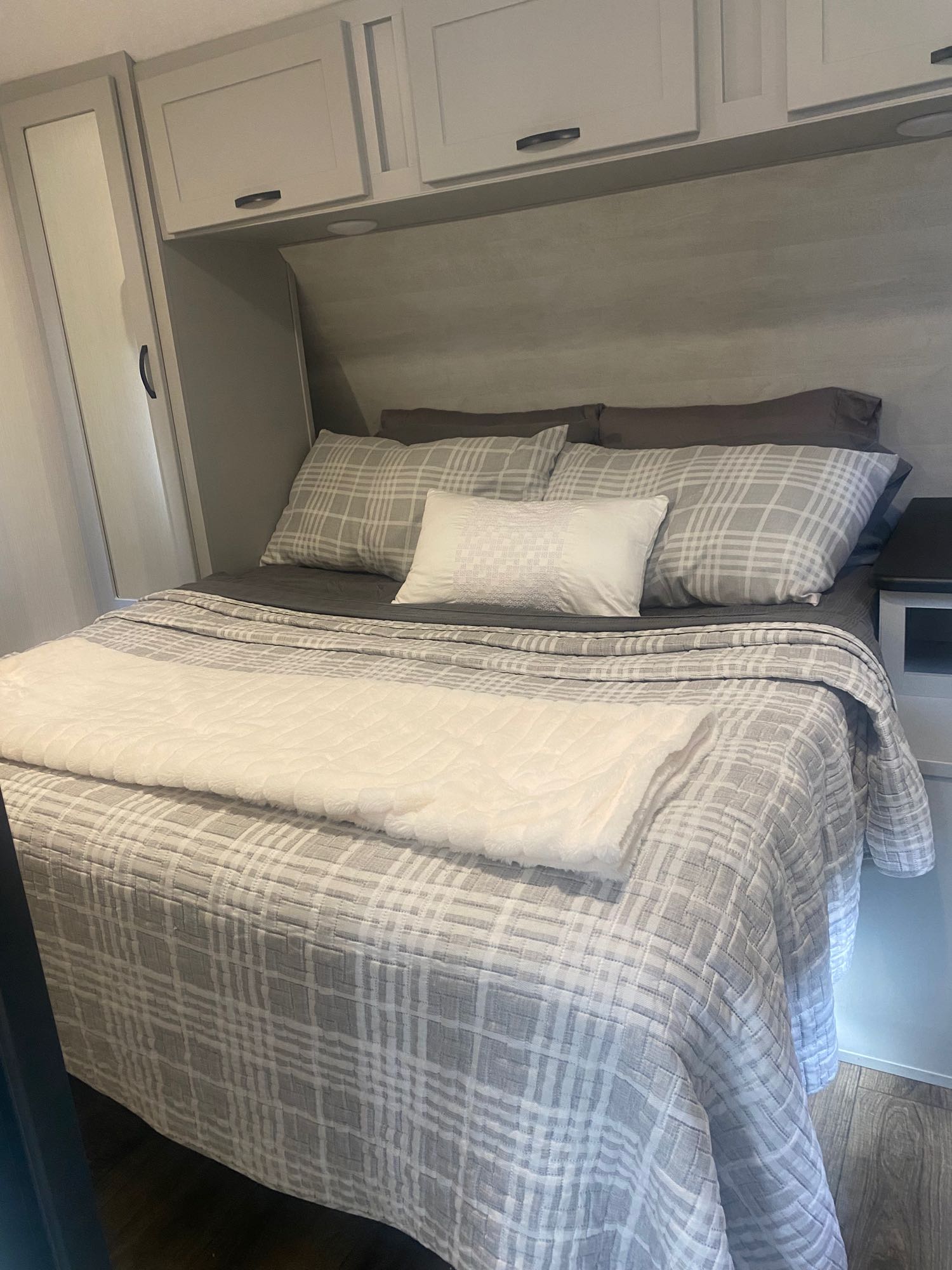 Inviting RV rental bedroom with neat gray plaid bedding, fluffy throw, overhead cabinets, and wardrobe. Perfect for your trip.. Forest River Vibe 2021
