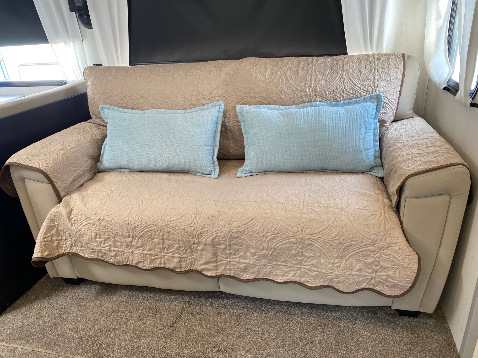 Comfortable RV rental couch with decorative beige quilted cover and two light blue pillows for travel comfort.. Forest River Vibe 2021