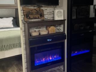 Interior of an RV rental showing a cozy bedroom, entertainment unit with an electric fireplace, and another fireplace to the right.. Forest River Wildwood 2020