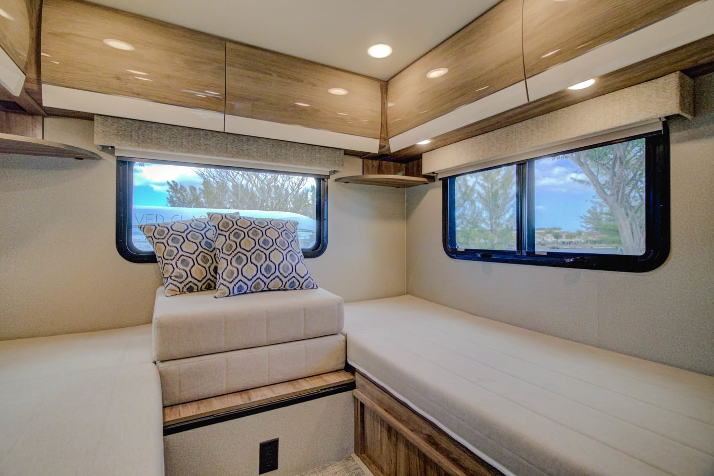 Cozy RV rental interior with light-colored sleeping benches, patterned pillows, windows, and overhead cabinets.. Entegra Coach Qwest 2020