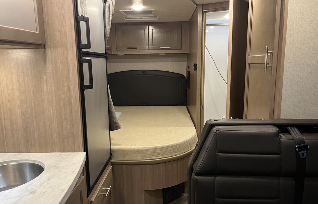 Spacious RV rental interior featuring a bed, kitchen sink, refrigerator, and an open bathroom door.. Adventurer Adventurer 23 RB 2023