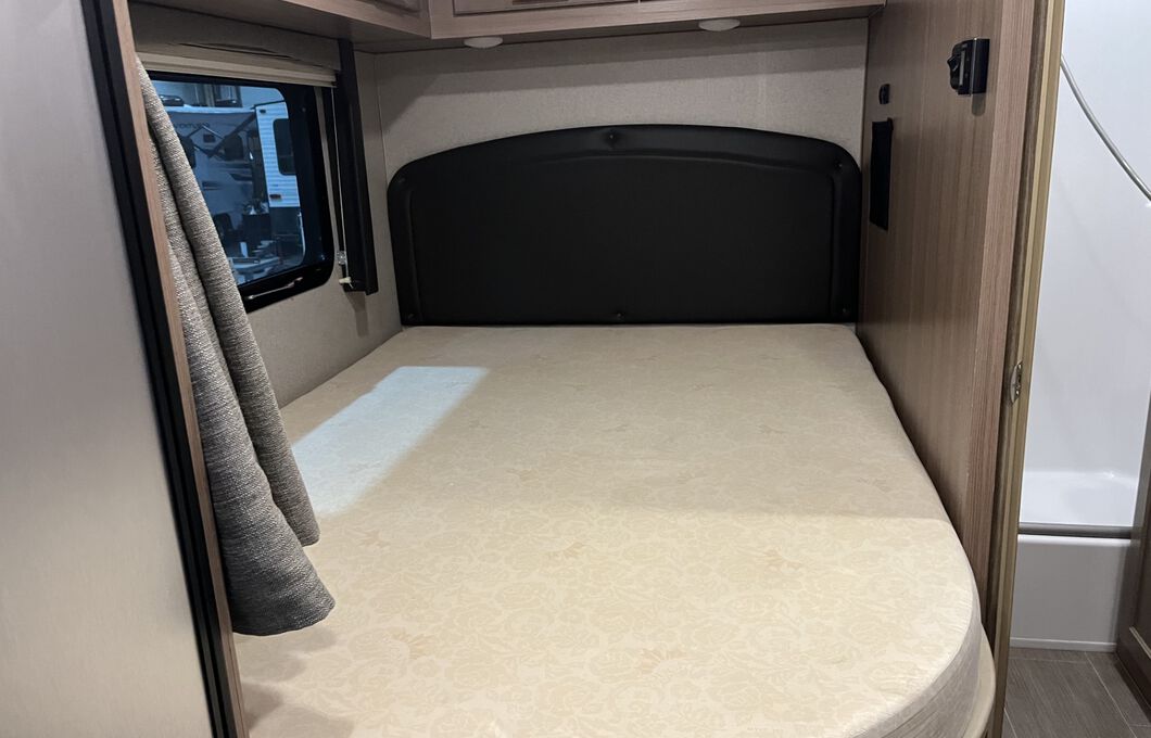 Cozy RV rental bedroom featuring a comfortable bed with a headboard, window, and attached small bathroom, ideal for travel.. Adventurer Adventurer 23 RB 2023