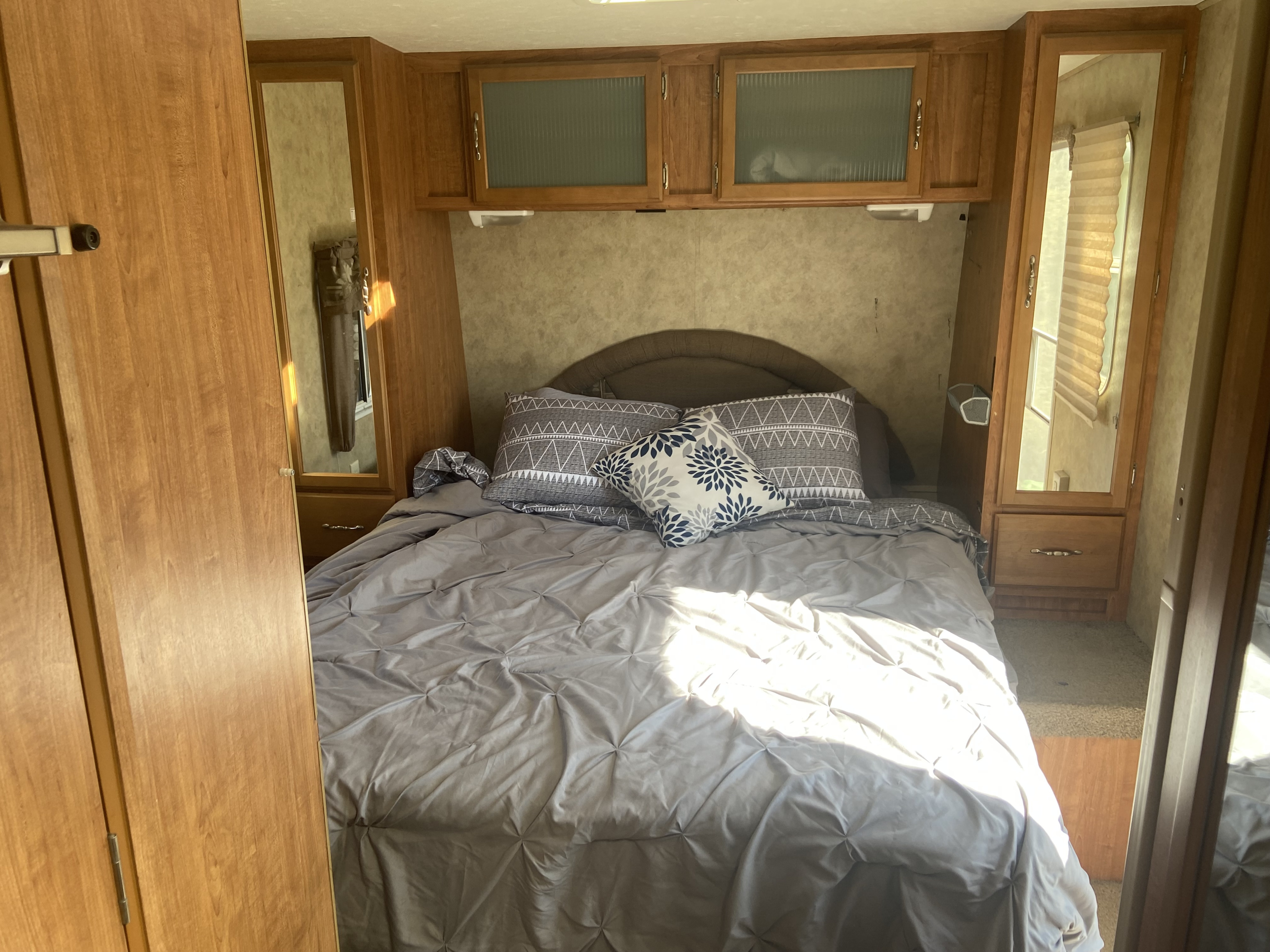 RV rental's compact bedroom features a bed with grey comforter & patterned pillows, overhead cabinets, and built-in storage.. Komfort Trailblazer 2008