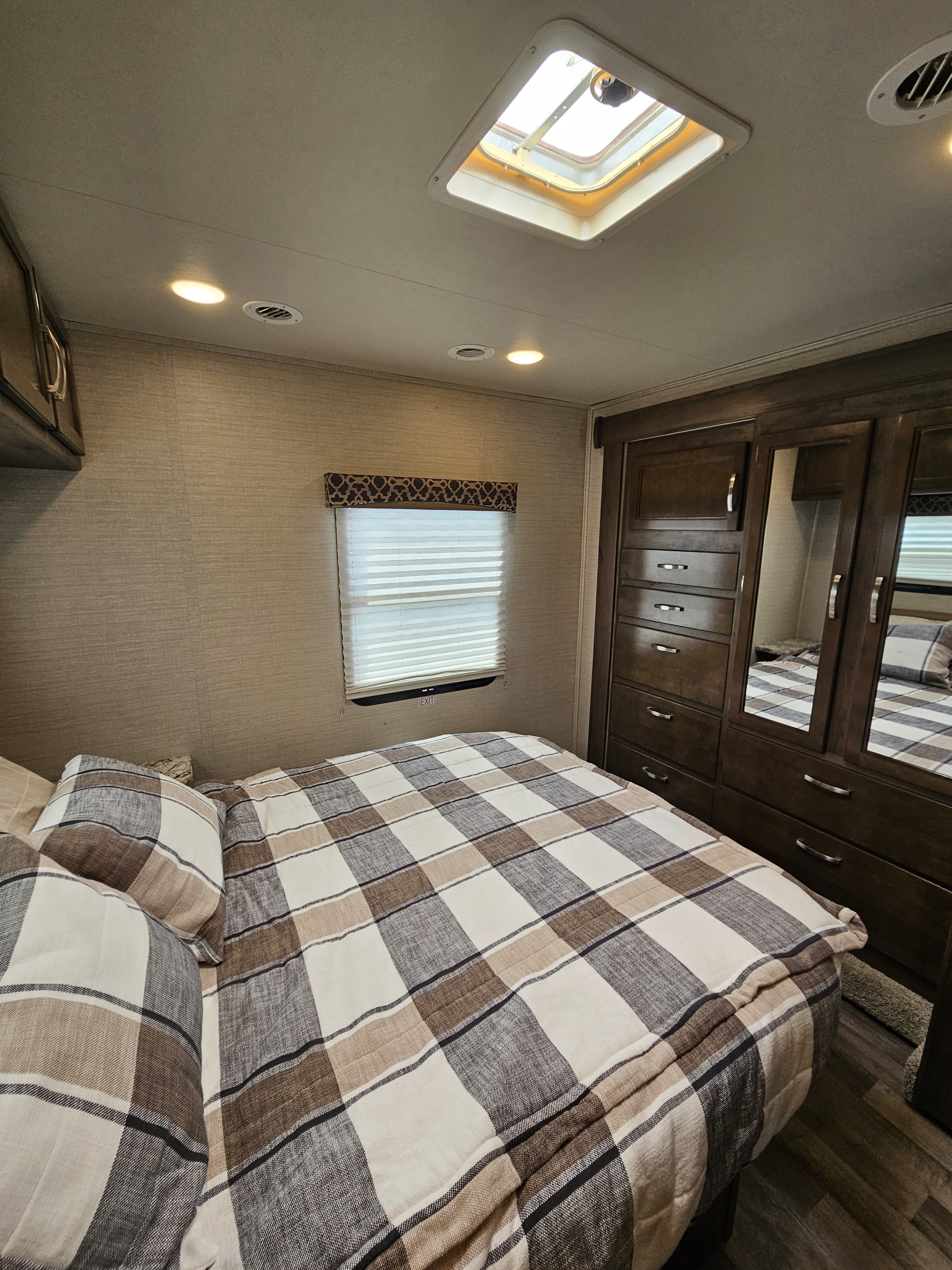 Cozy RV rental bedroom featuring plaid bedding, mirrored wardrobe, and a skylight for a bright, comfortable stay.. Jayco Redhawk 2020