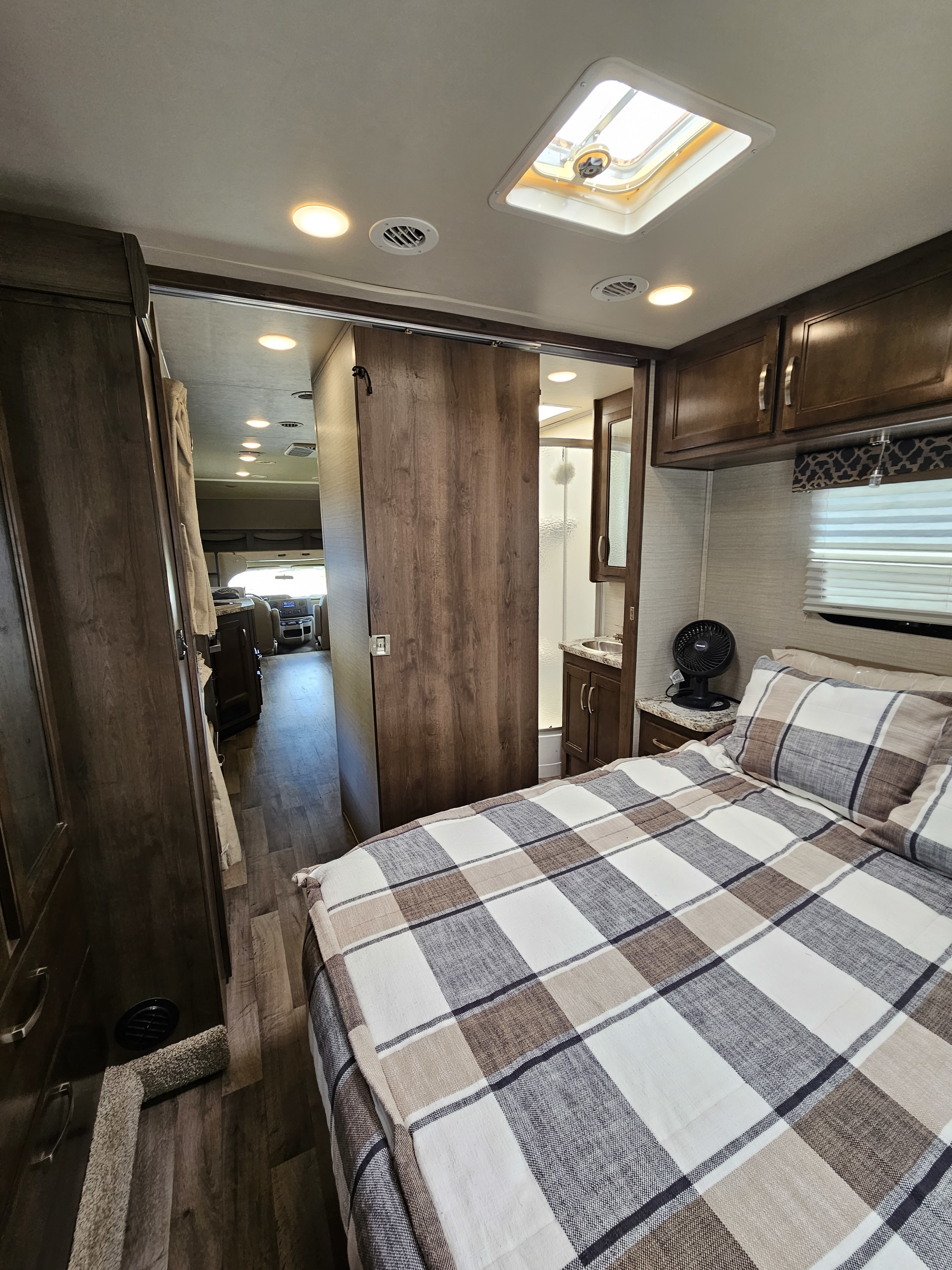 Spacious RV rental bedroom with cozy plaid bedding, private bath, and access to the main living area of the motorhome.. Jayco Redhawk 2020