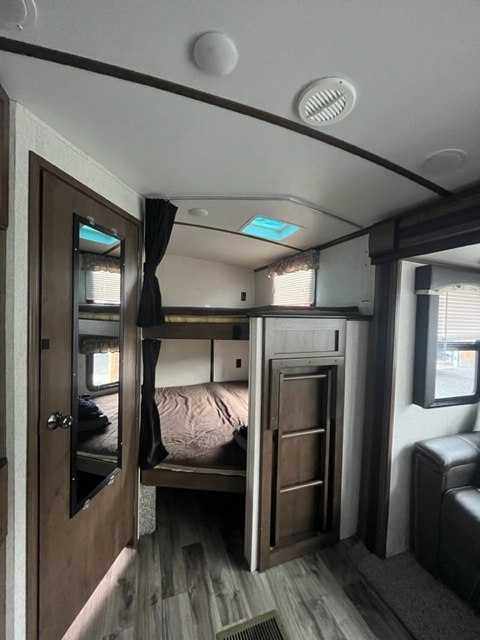 Inside this RV rental, two bunk beds with privacy curtains are visible. A skylight brightens the wood-look floor living area.. Keystone RV Cougar 2018