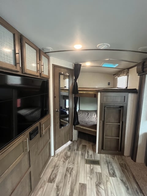 Inside an RV rental: a spacious bunk bed area with ladder, entertainment center, and modern wood-look flooring.. Keystone RV Cougar 2018