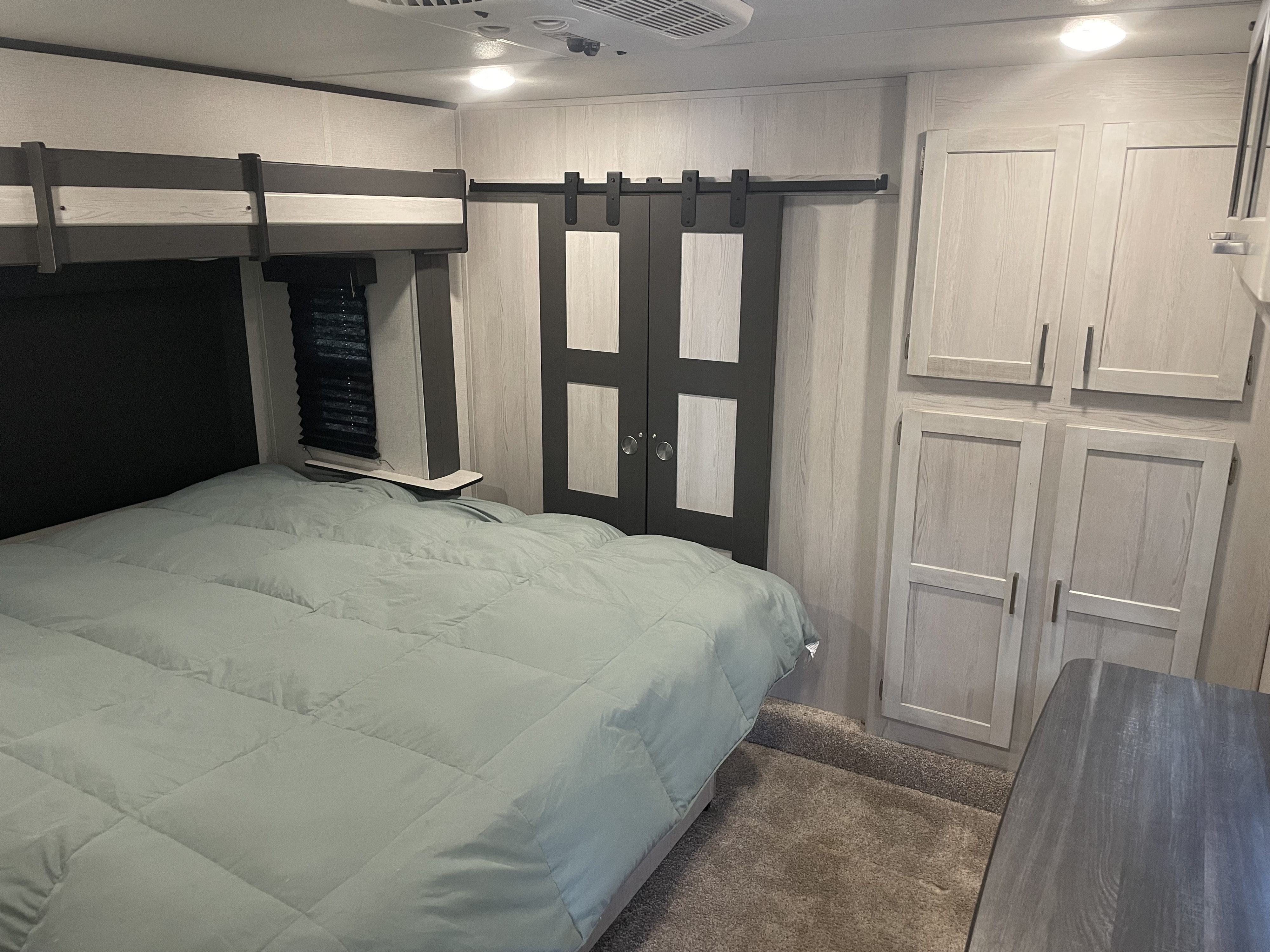 Cozy RV rental bedroom featuring a large bed, overhead bunk, sliding closet doors, and storage cabinets.. Keystone RV Sprinter Limited 2020