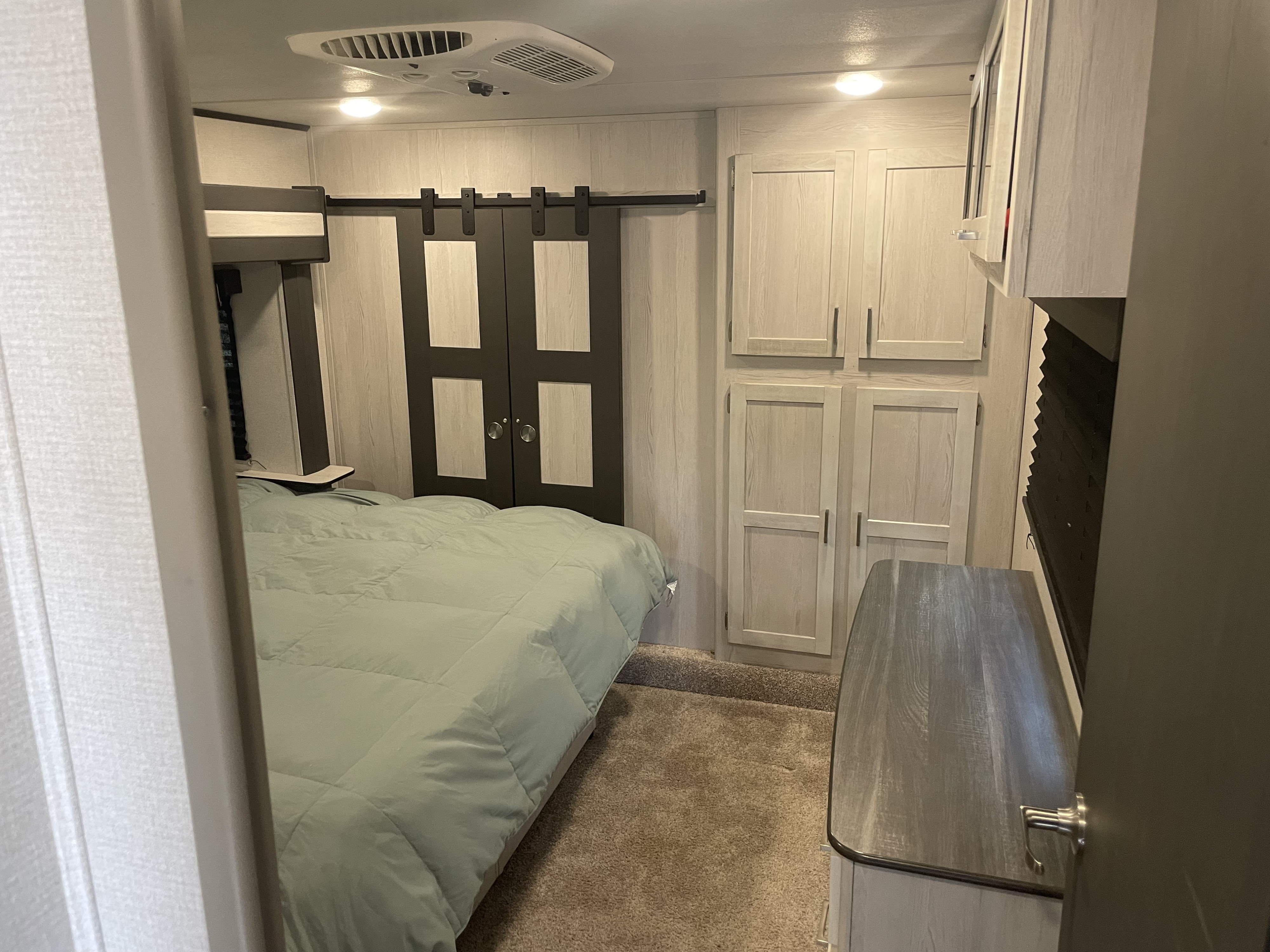 Step into this cozy RV rental bedroom. It features a bed, barn door wardrobe, overhead cabinets, and a dresser, maximizing space.. Keystone RV Sprinter Limited 2020