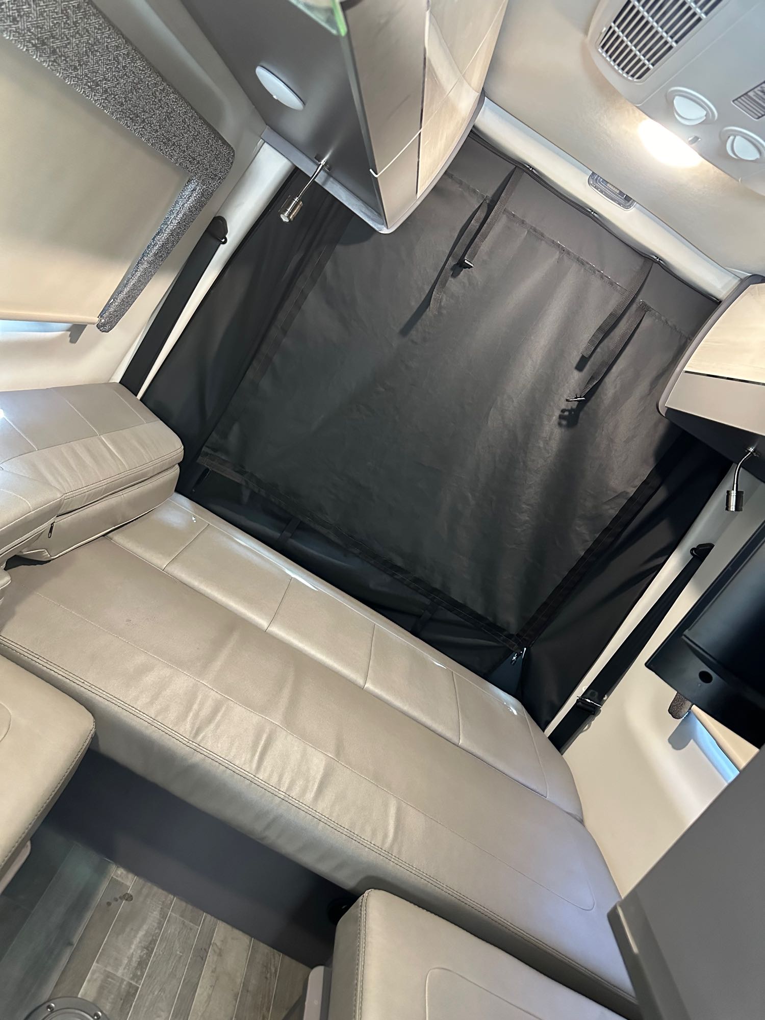 Inside an RV rental: A light-colored bench seat and dark privacy curtain offer comfort & shade for travel.. Mercedes-Benz Sprinter RV Motorhome Campervan 2023