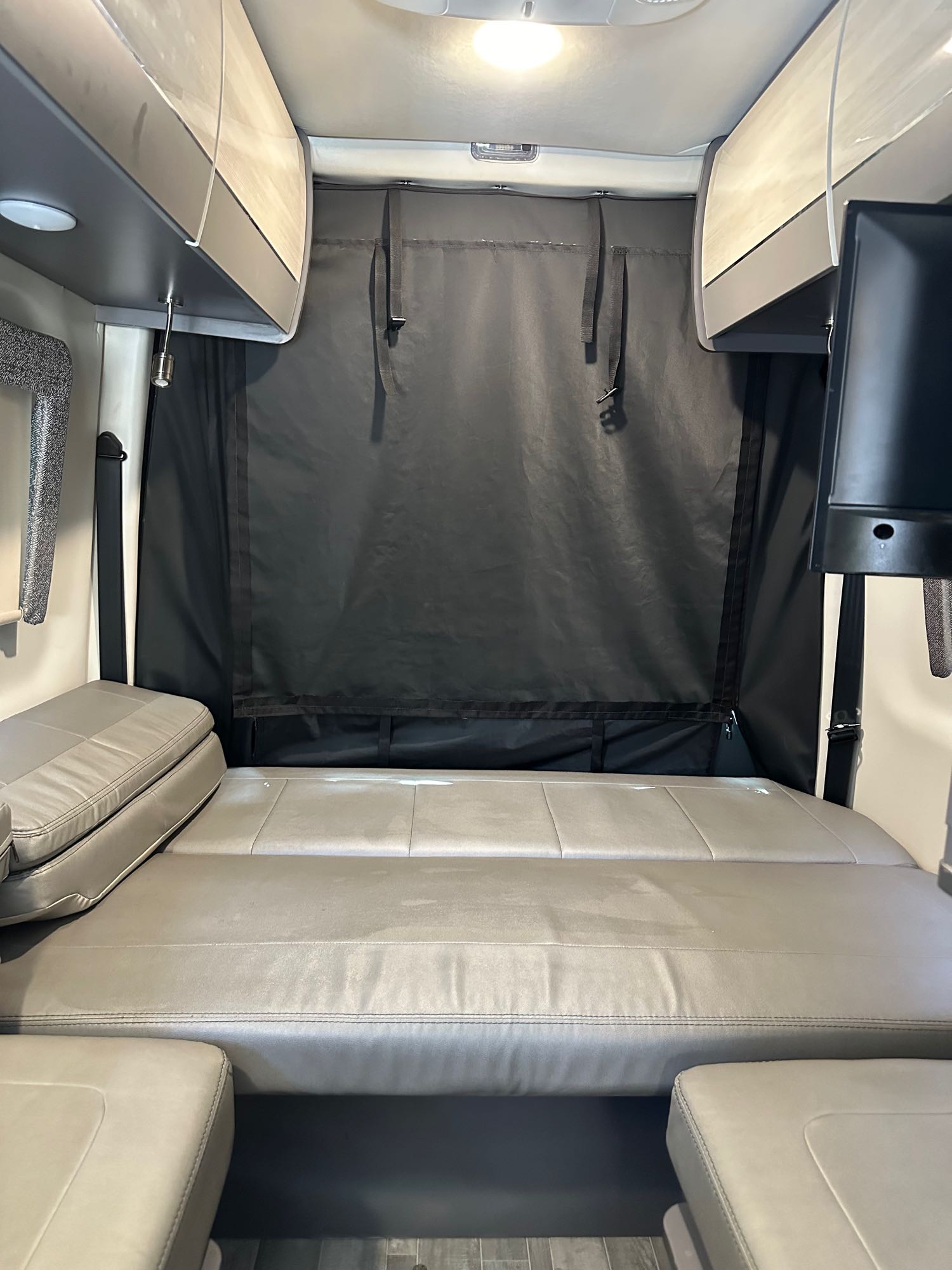 Spacious RV rental interior featuring a comfy bed, overhead storage, privacy curtain, and TV, perfect for your next road trip.. Mercedes-Benz Sprinter RV Motorhome Campervan 2023