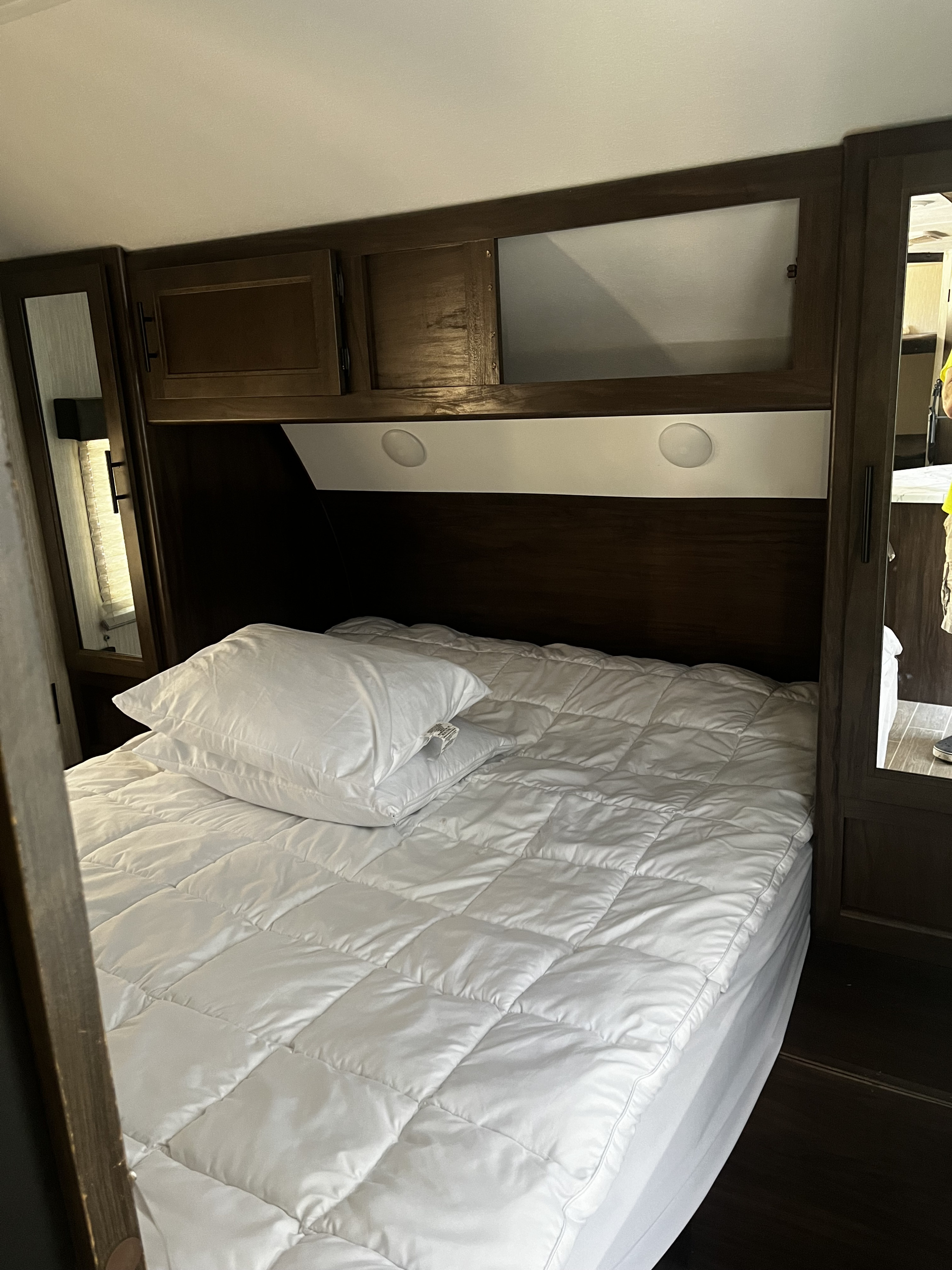 Cozy RV rental bedroom with white quilted bedding, pillows, and dark wood overhead cabinets. Ideal for compact travel.. Forest River Cherokee Grey Wolf 2020