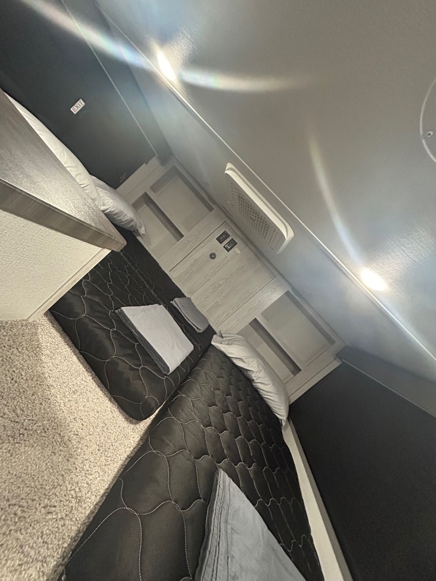Inside a modern rv rental bedroom: two quilted beds, built-in storage, and an overhead EXIT sign.. Keystone RV Montana High Country 2023