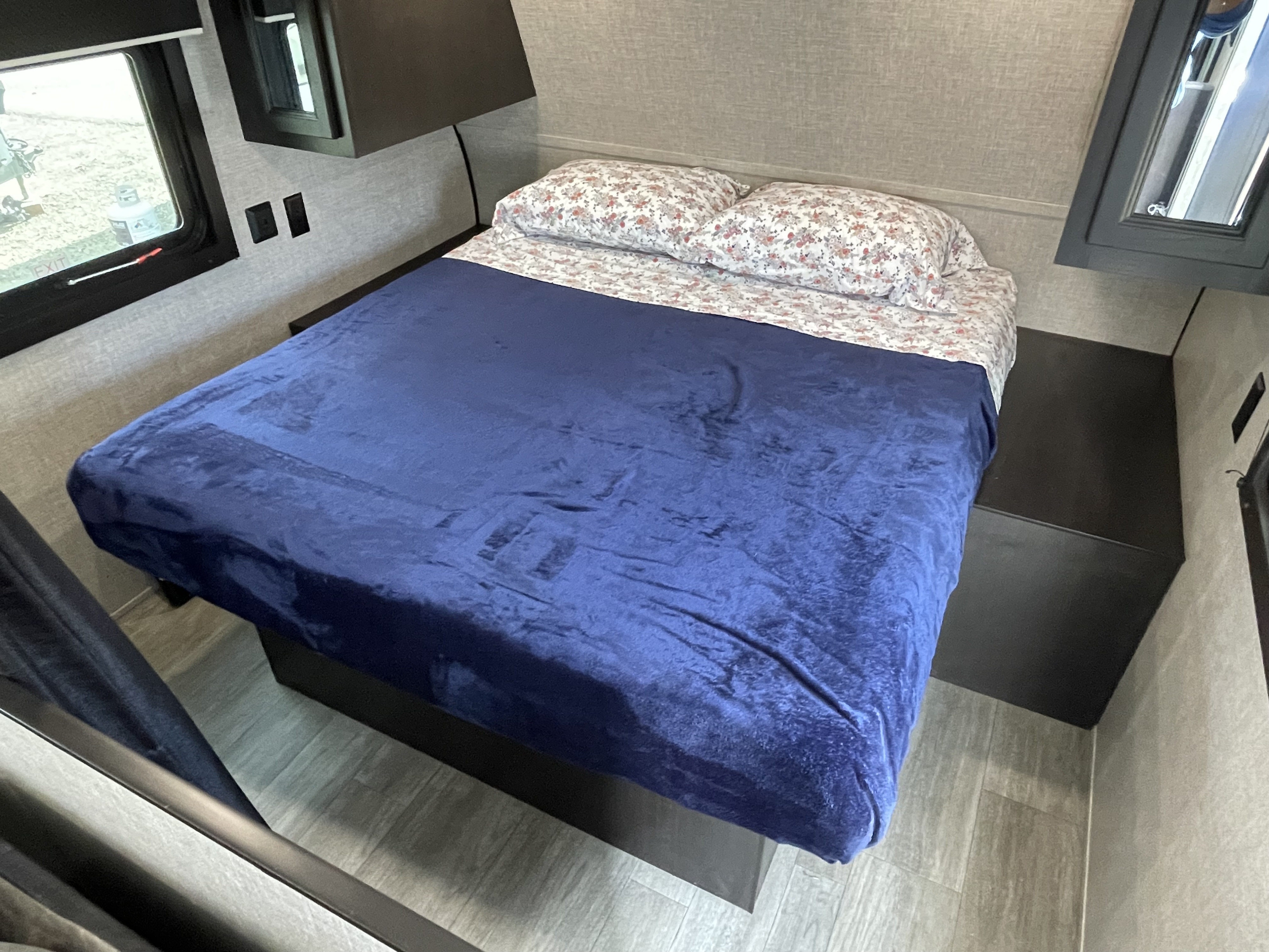 Inside an RV rental, a compact bedroom features a bed with blue blanket, floral pillows, and integrated storage.. Jayco Jay Flight 2022