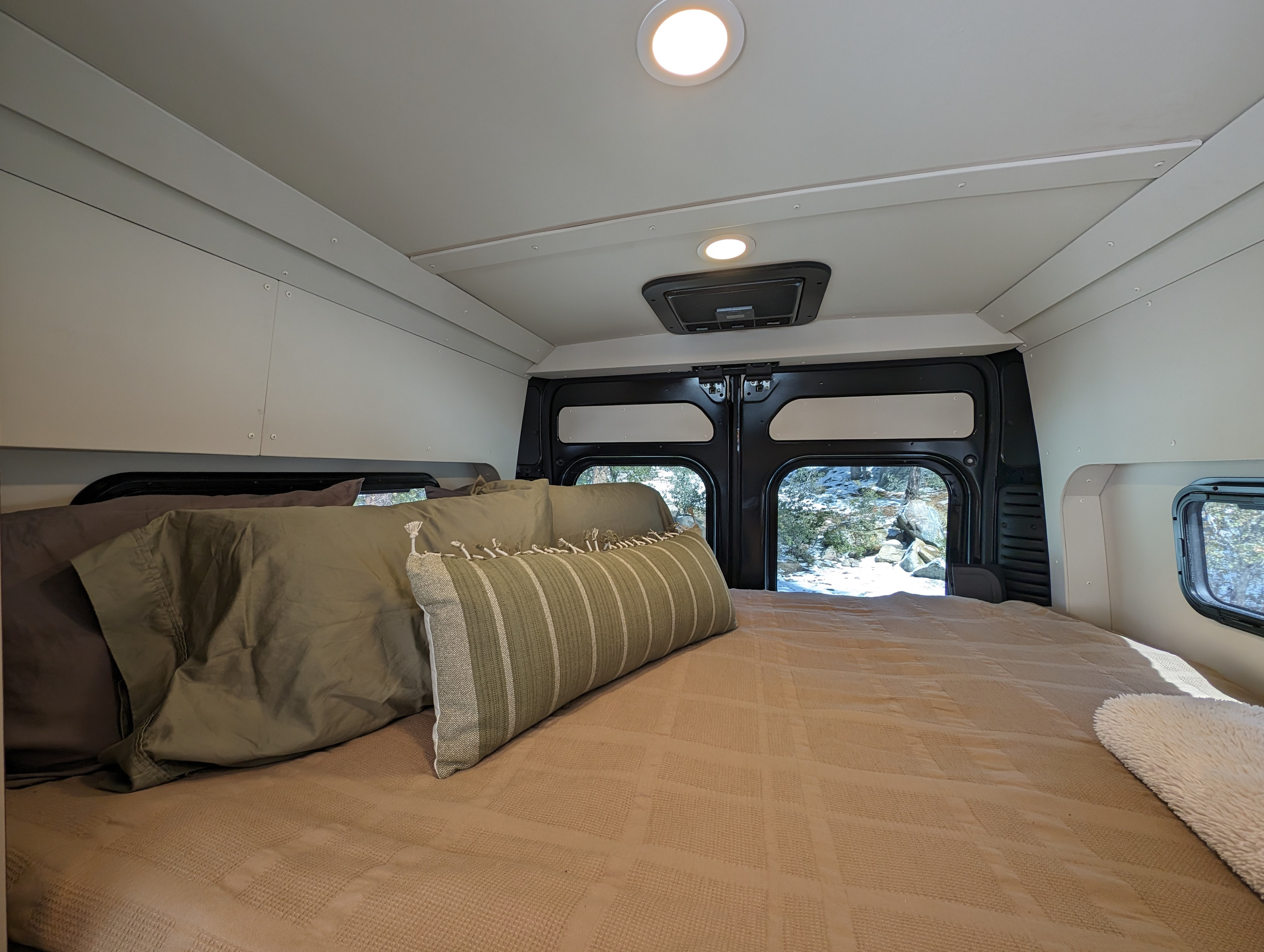 Cozy RV rental bed with a snowy view out the back doors. Ideal for winter getaways.. New Life Conversions Luxury Edition 2022