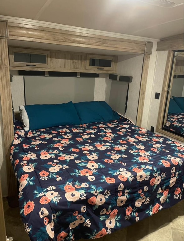 Cozy RV rental bedroom featuring a floral comforter on the bed, overhead storage cabinets, and a side mirror.. Palomino Solaire 2021